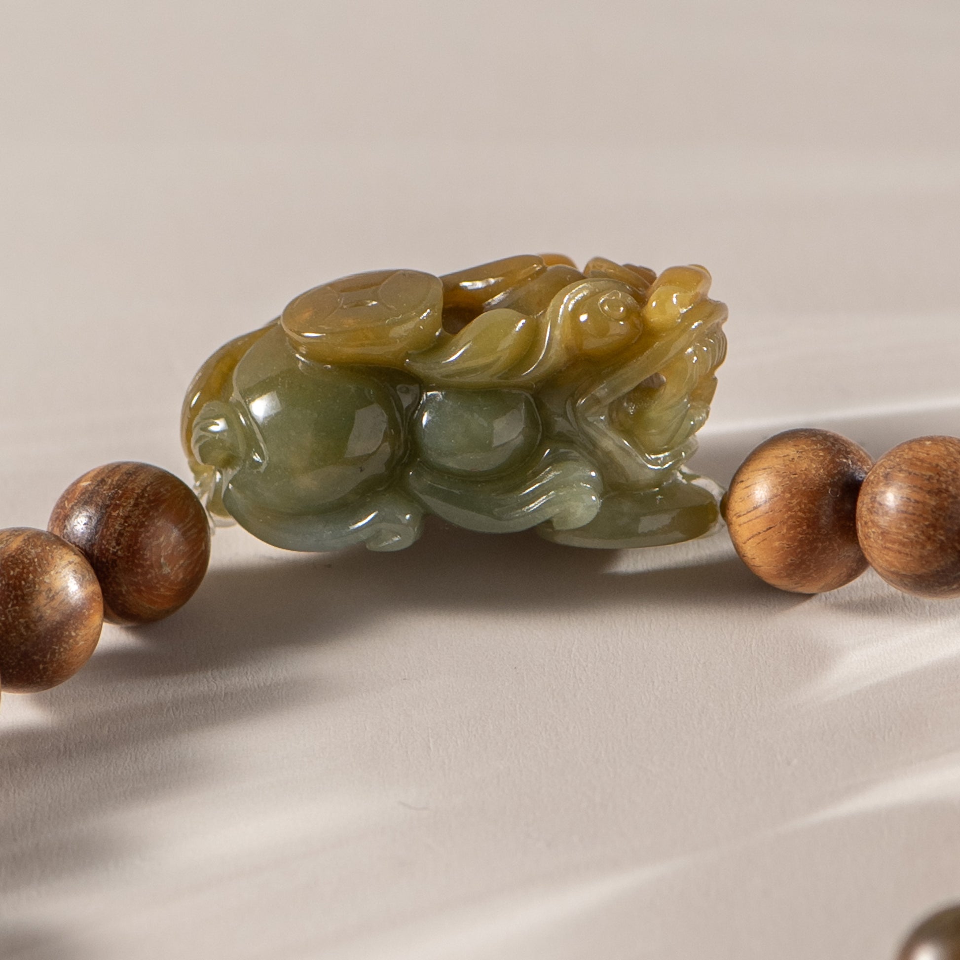 Carved jade piece with wooden beads on a beige background