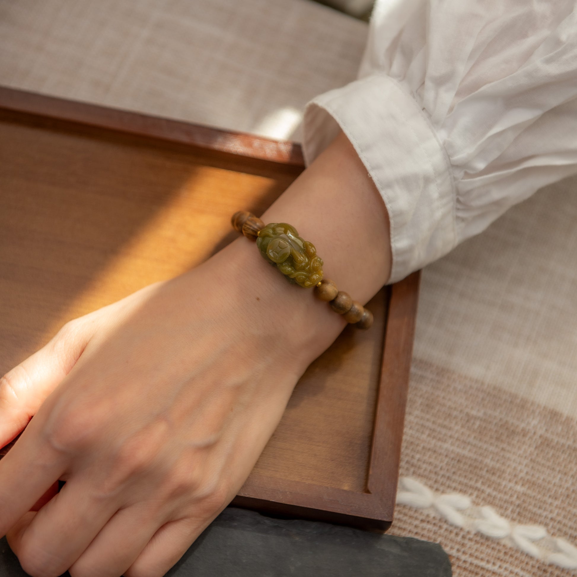 Hand wearing a bracelet with a green stone on a wooden surface