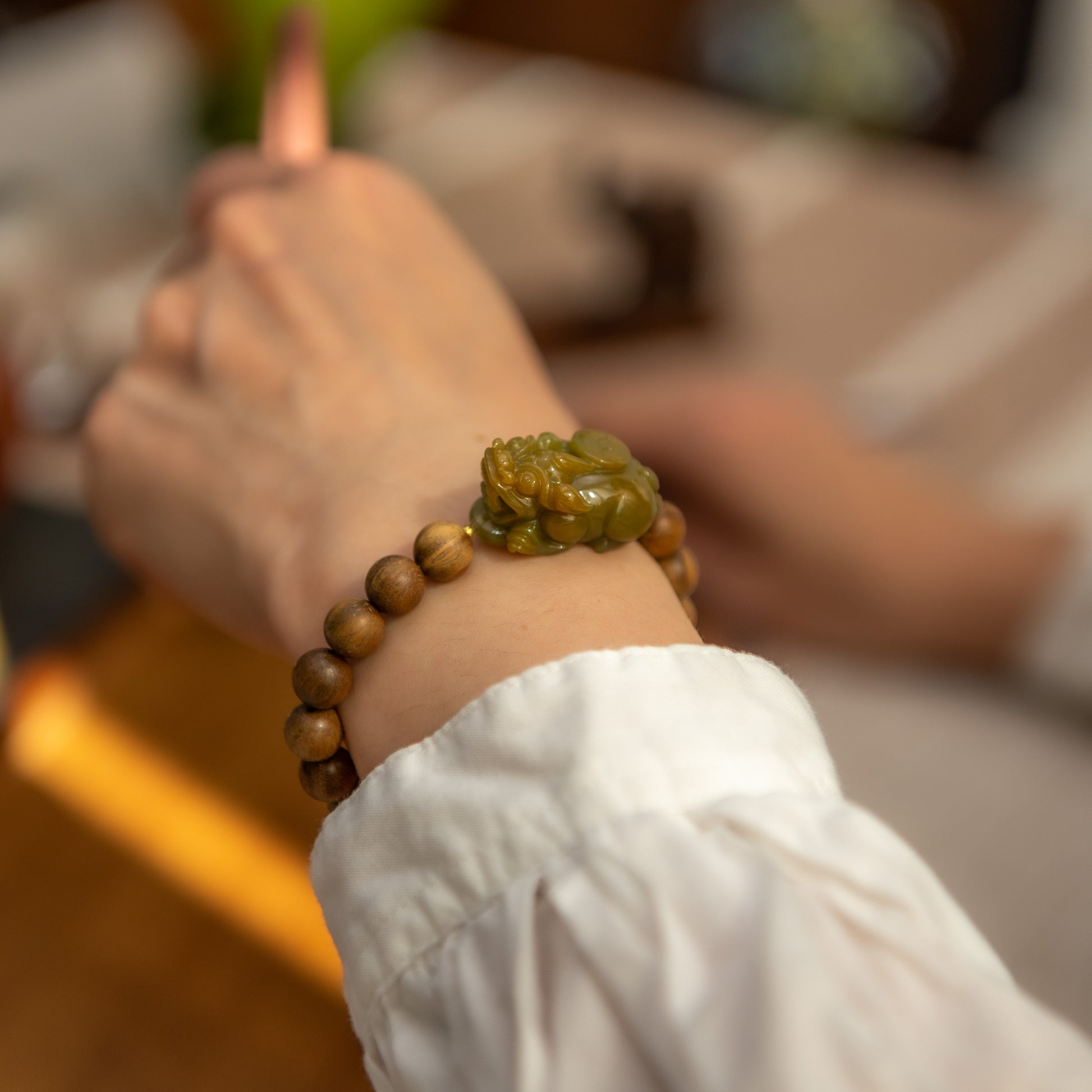 Close-up of a hand wearing a bracelet with wooden beads and a green stone.