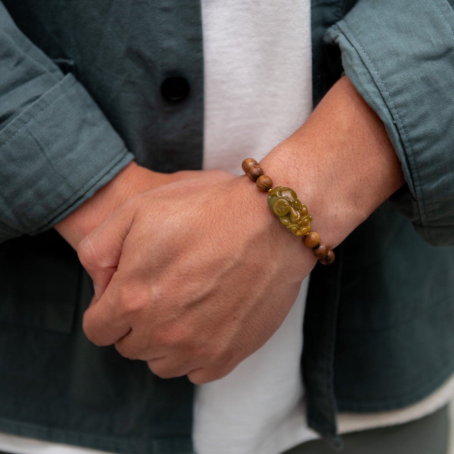 Close-up of a person wearing a bracelet with a green stone on a neutral background