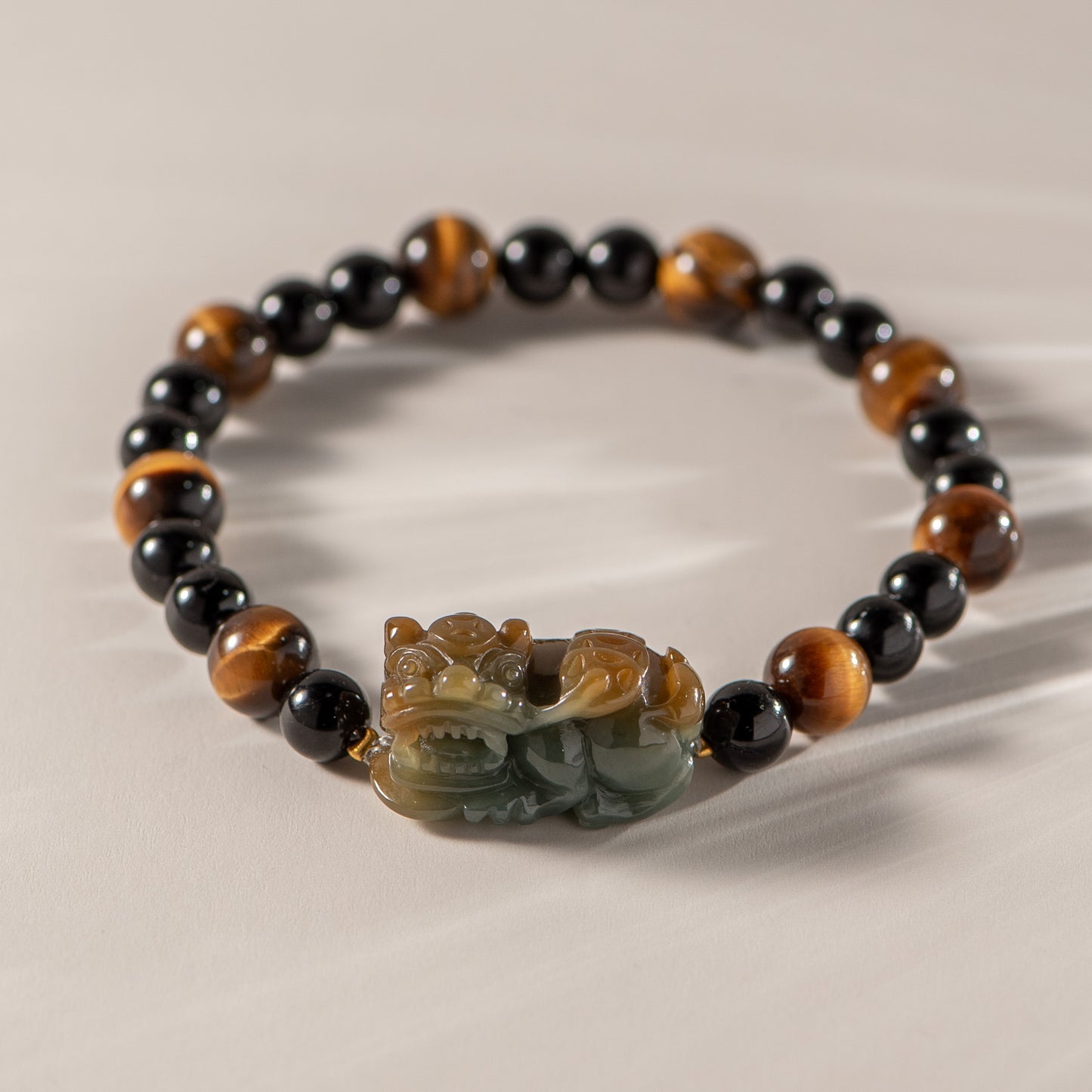Bracelet with black, brown, and green beads featuring a carved stone dragon charm on a beige background.