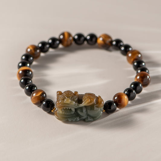 Bracelet with black, brown, and green beads featuring a carved stone dragon charm on a beige background.