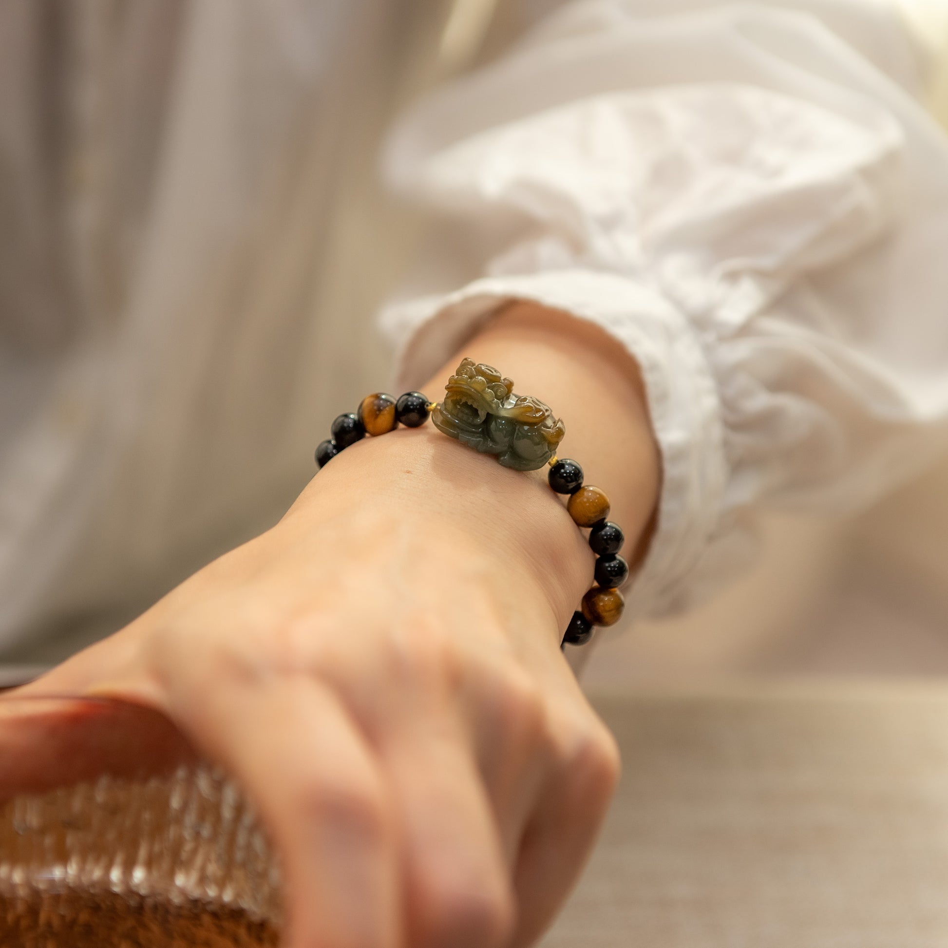 Close-up of a hand wearing a bracelet with natural stone beads on a neutral background