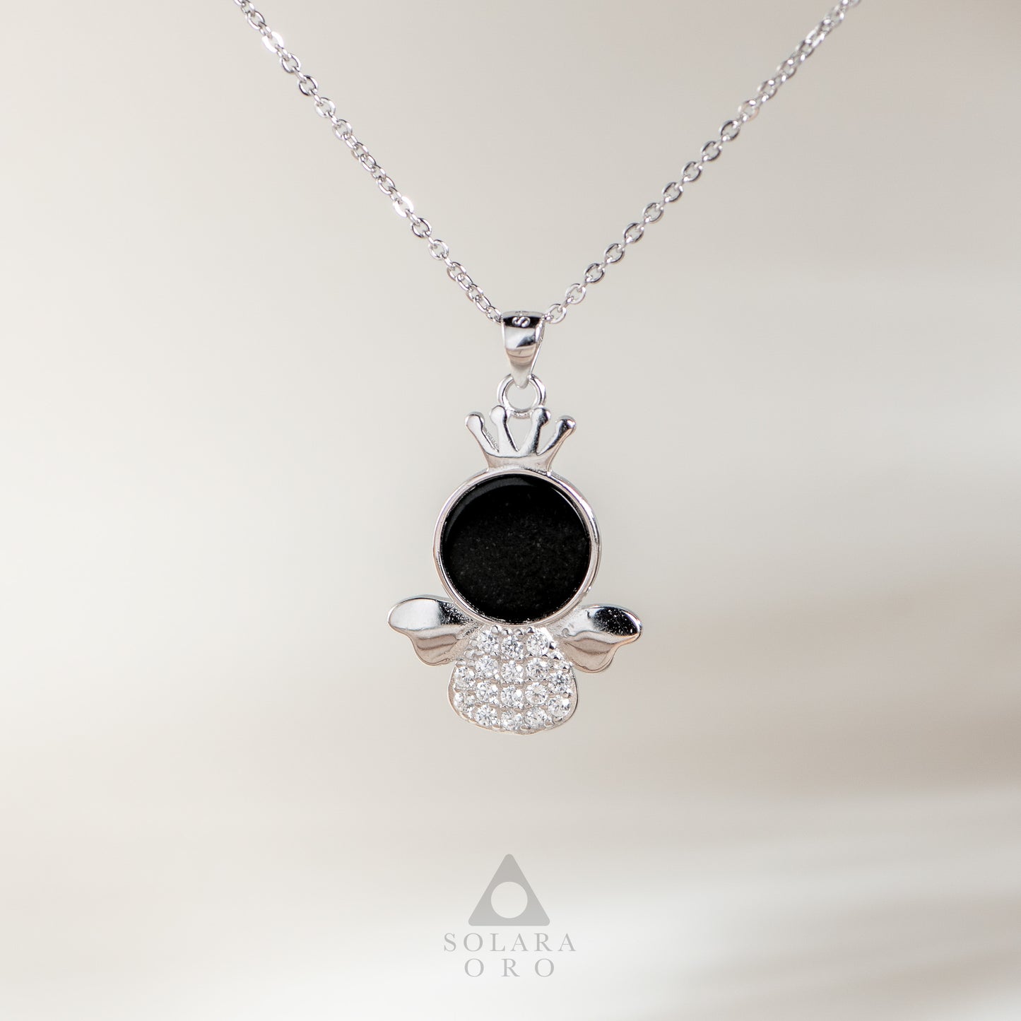 Silver pendant with black center and clear stones on a white background, featuring Solara Oro logo.