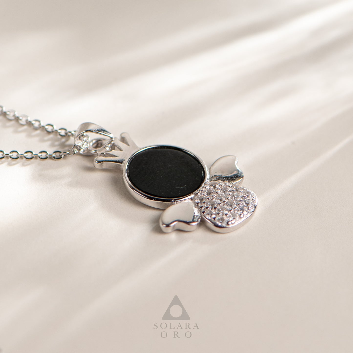 Silver necklace with a black pendant on a white satin background, featuring the Solara Oro brand.