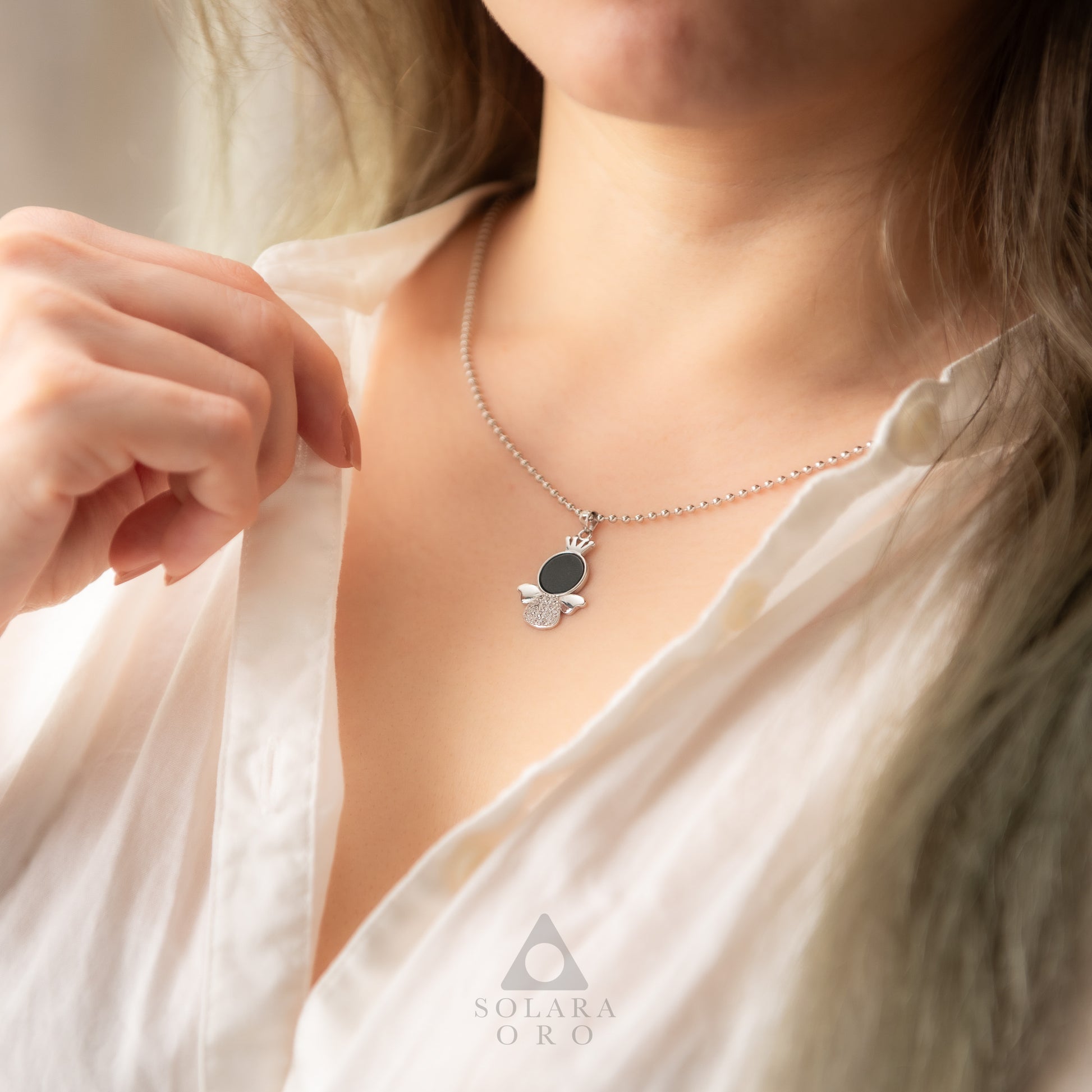 Person wearing a necklace with a hamsa pendant, branded 'SolaRara Oro'.