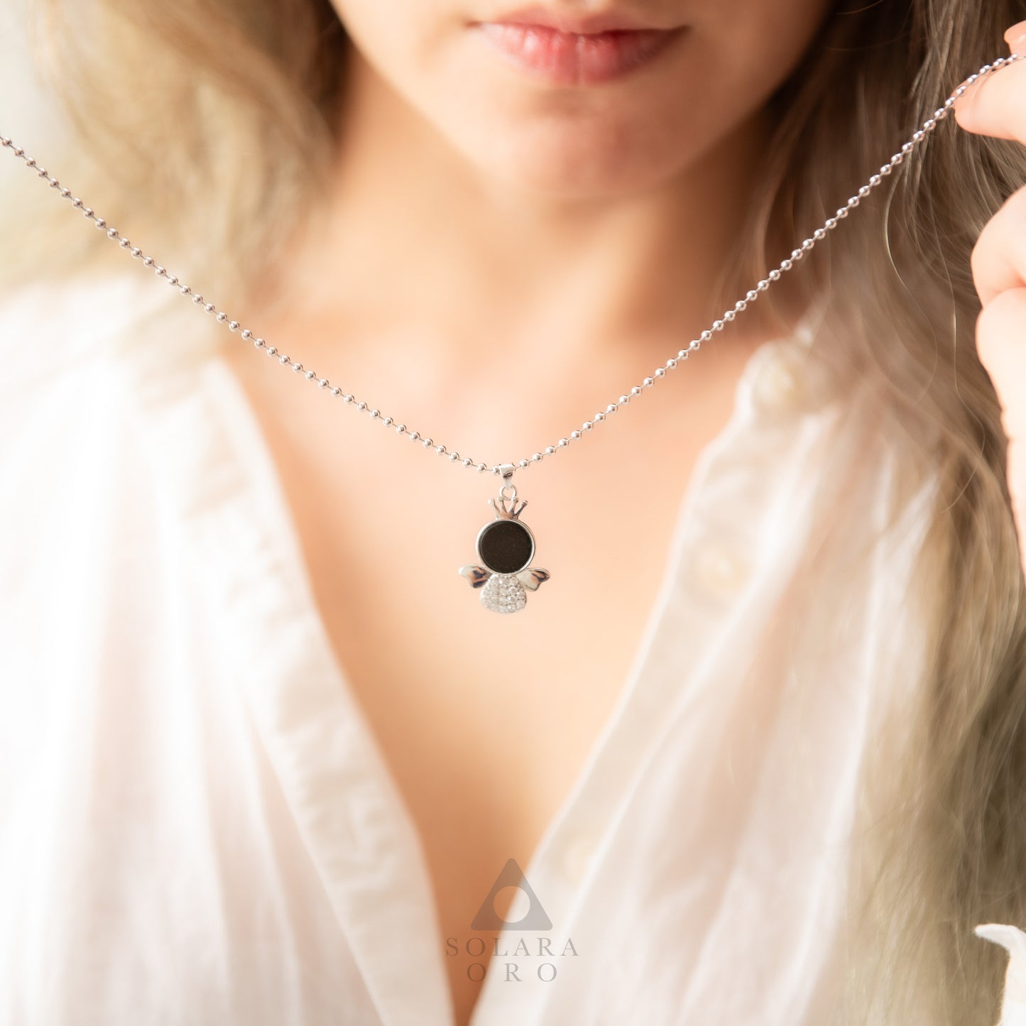 Close-up of a necklace with a pendant worn by a person, brand 'Sylva & Rudi' visible.