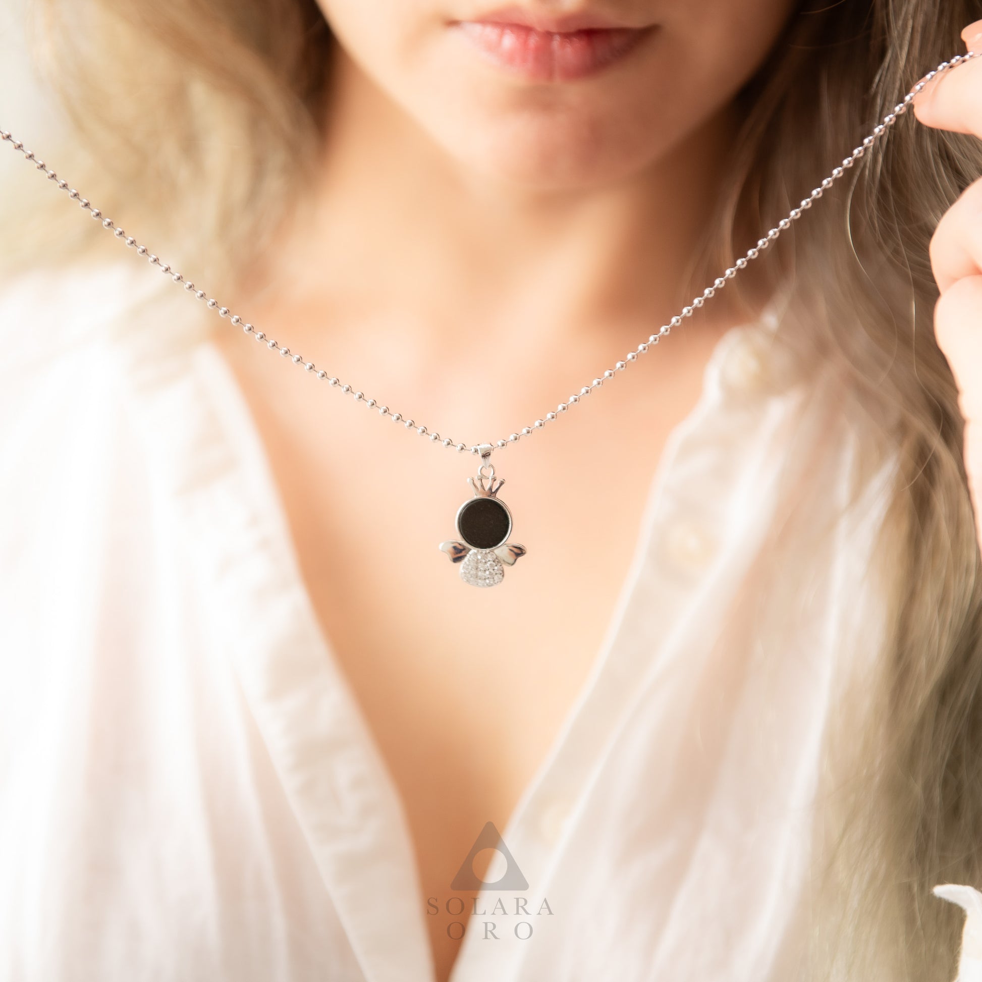 Close-up of a necklace with a pendant worn by a person, brand 'Sylva & Rudi' visible.