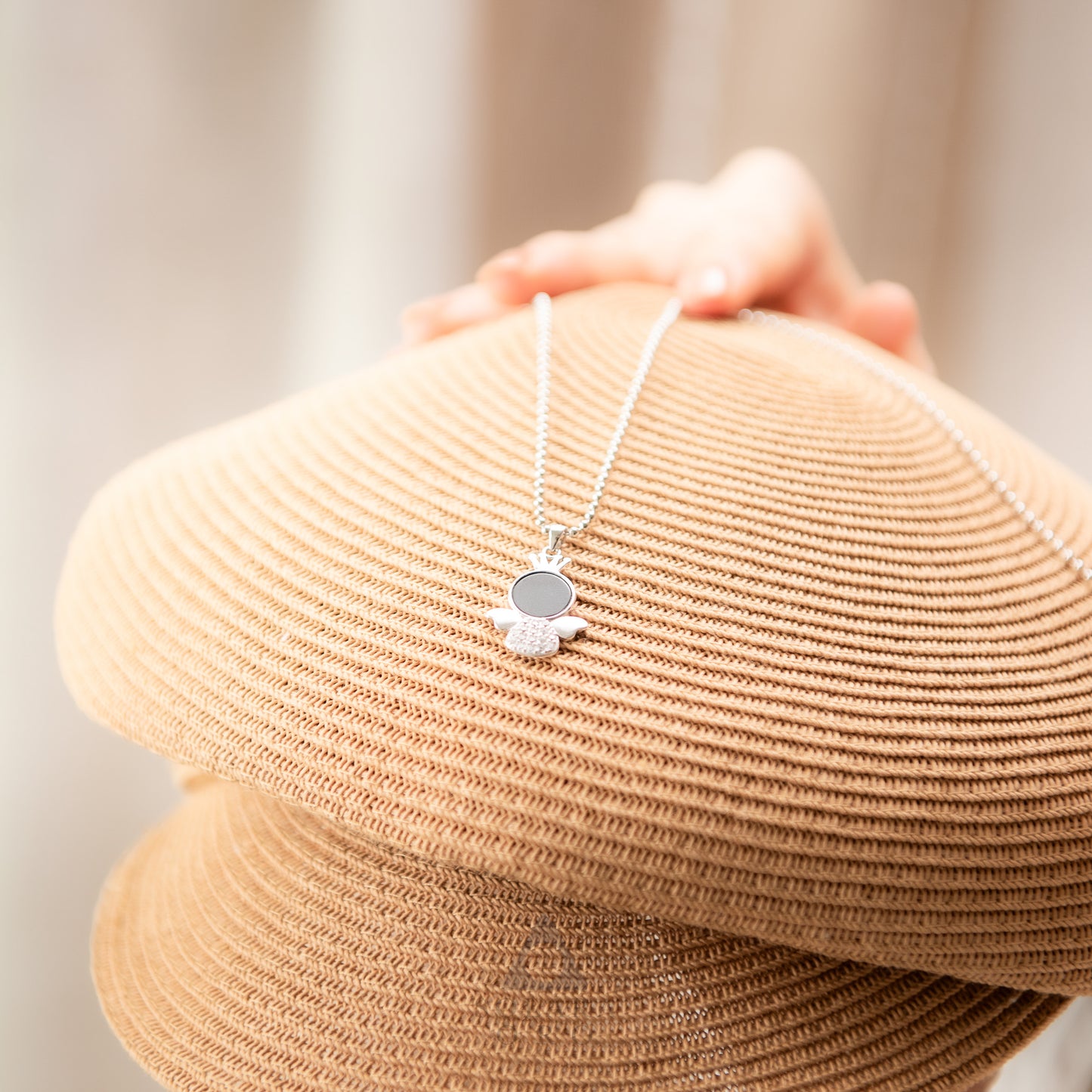 Necklace with a pendant held over a beige hat on a neutral background
