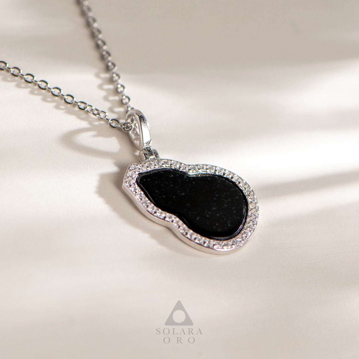 Necklace with a black pendant and diamond accents on a beige background, featuring the brand 'Soleara Oro'.