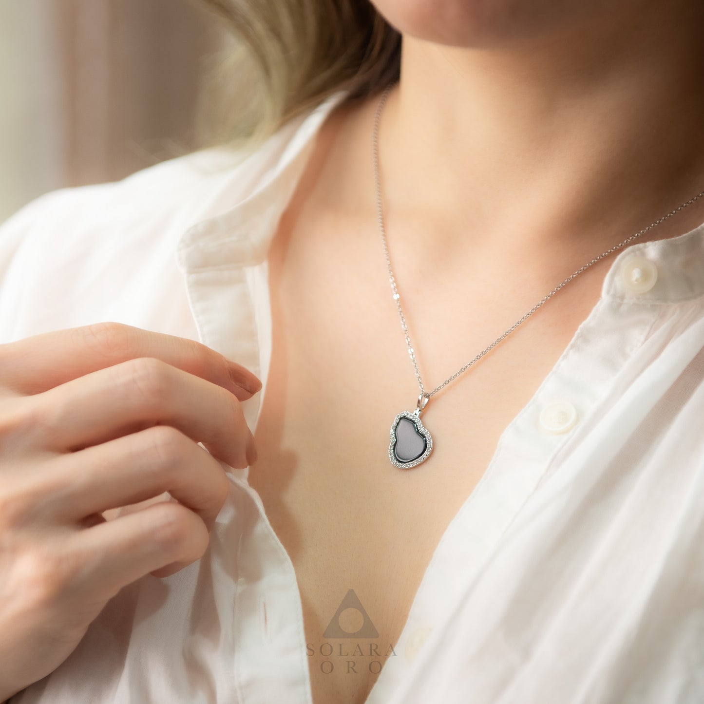 Person wearing a silver necklace with a heart-shaped pendant on a blurred background