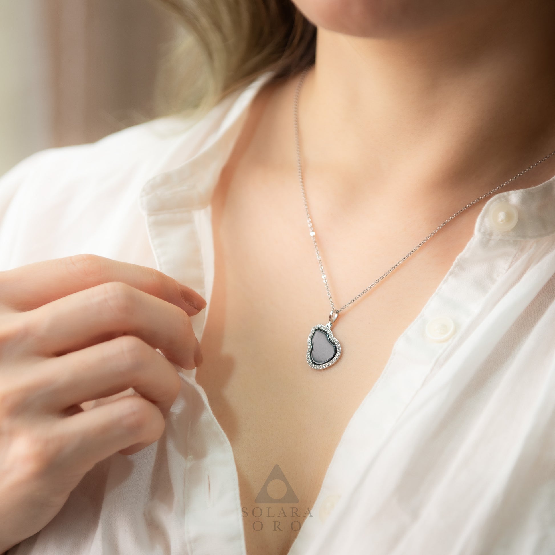 Person wearing a silver necklace with a heart-shaped pendant on a blurred background