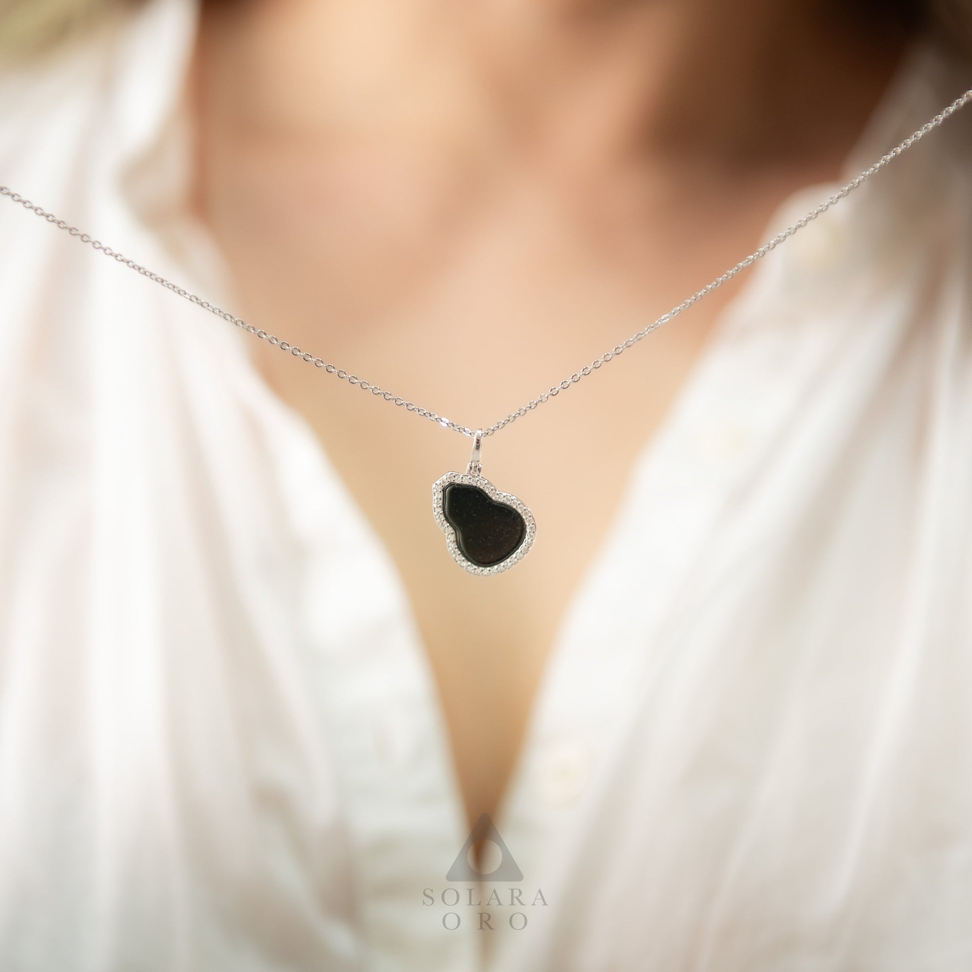 Necklace with a black pendant worn by a person in a white shirt, brand 'Soleara Oro' visible.