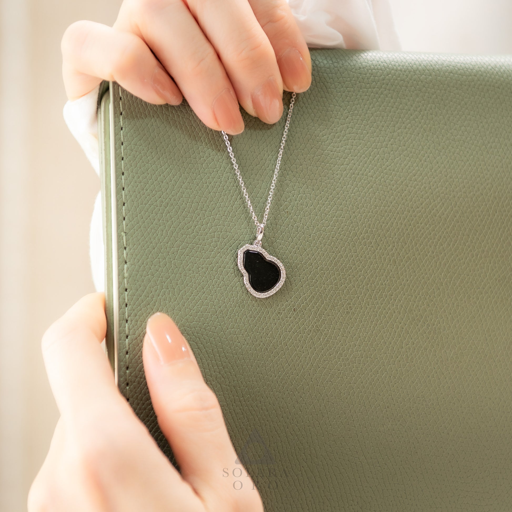 Necklace with a heart-shaped pendant held by hands against a green background