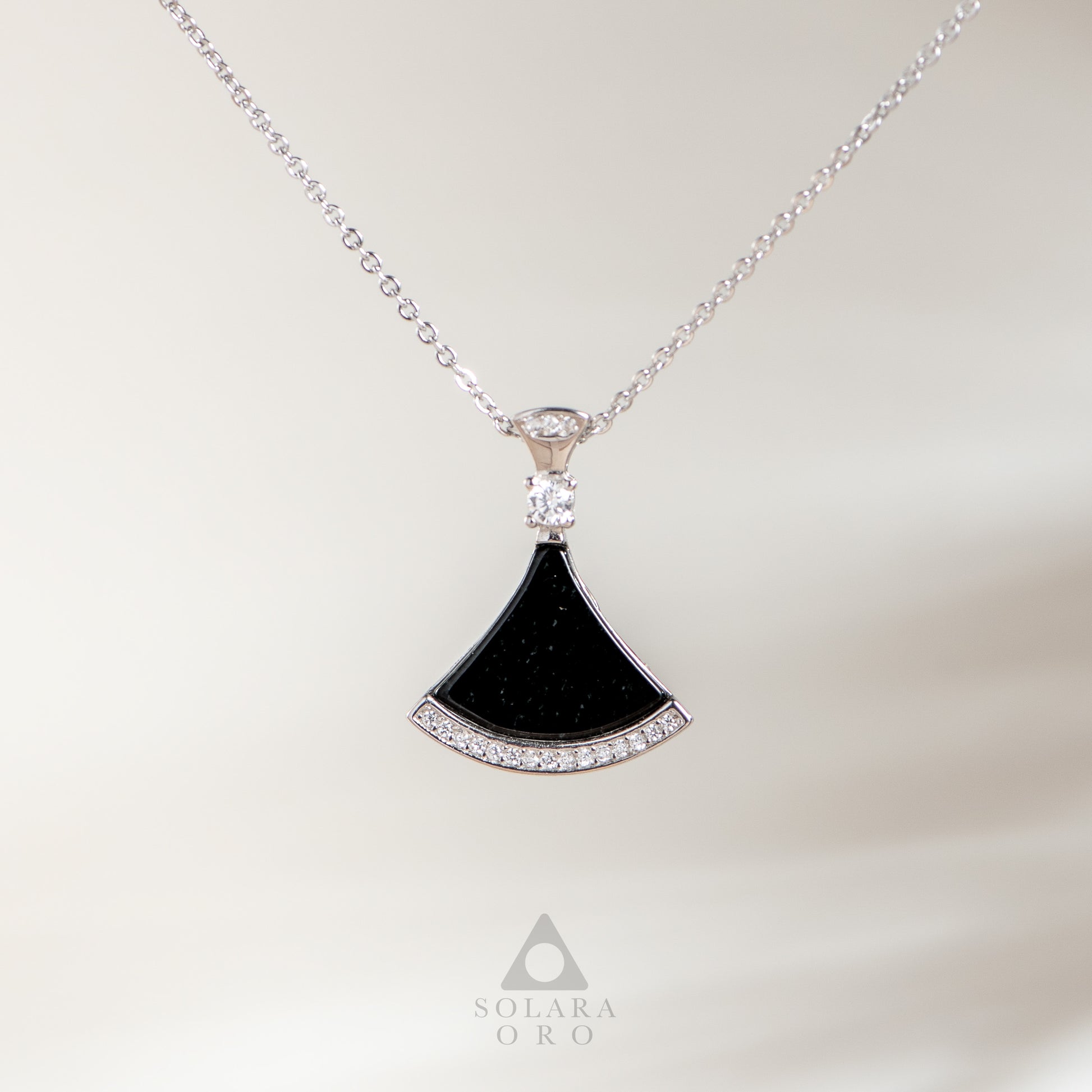 Black fan-shaped pendant with diamonds on a silver chain against a white background, featuring the Solara Oro logo.