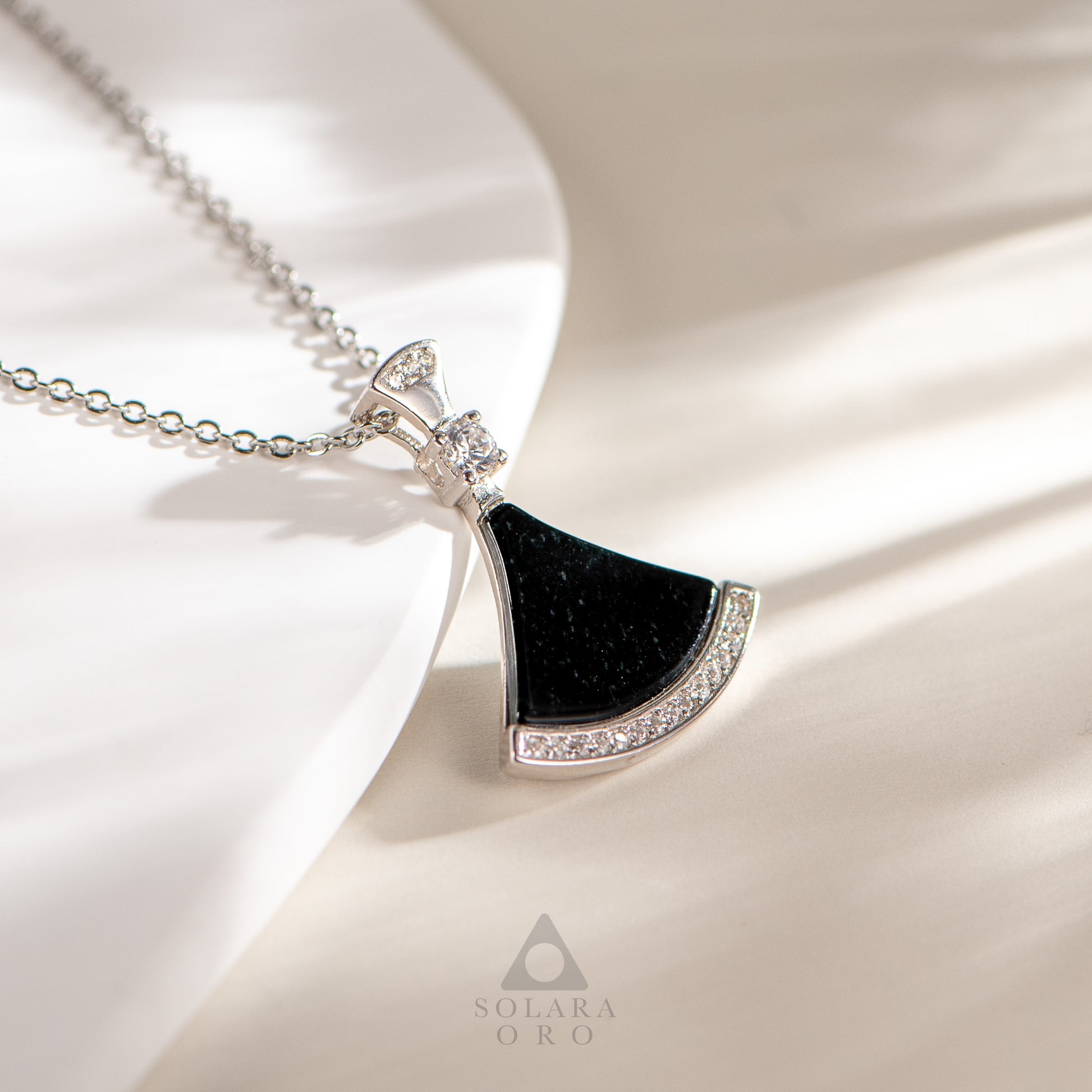 Necklace with a black pendant and diamond accents on a white fabric background, featuring the brand 'Solara Oro'.