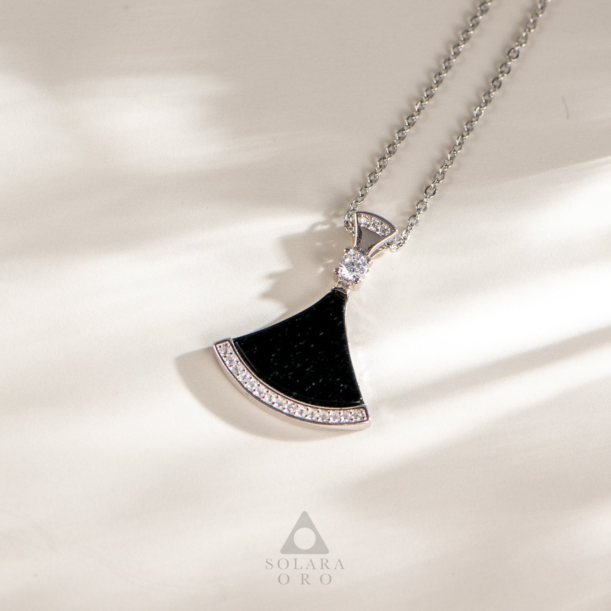 Black fan-shaped pendant necklace with chain on a light background, featuring the Solara Oro brand.