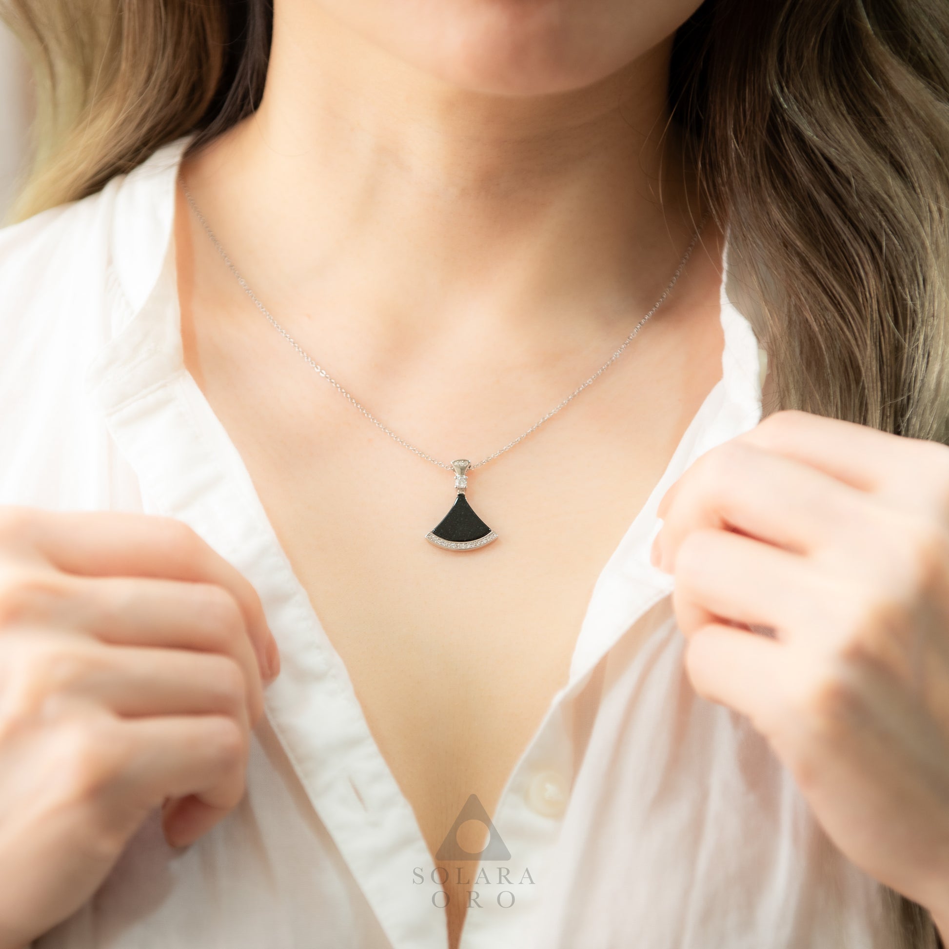 Person wearing a necklace with a unique pendant, brand 'Solara Oro' visible.