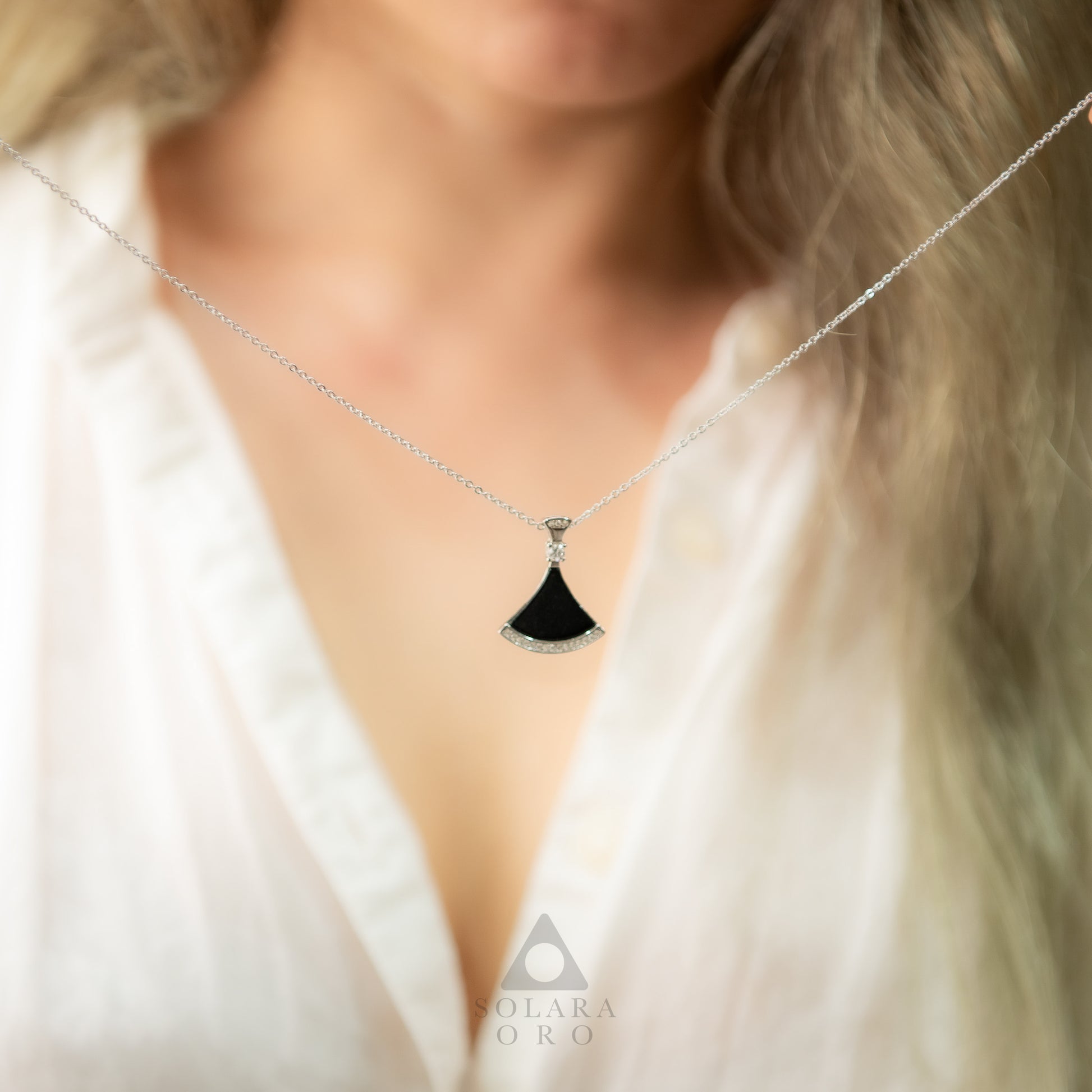 Necklace with a black pendant worn by a person, brand 'Solara Oro' visible.