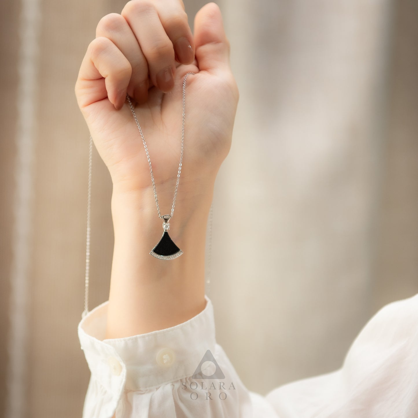 Hand wearing a necklace with a black pendant against a neutral background