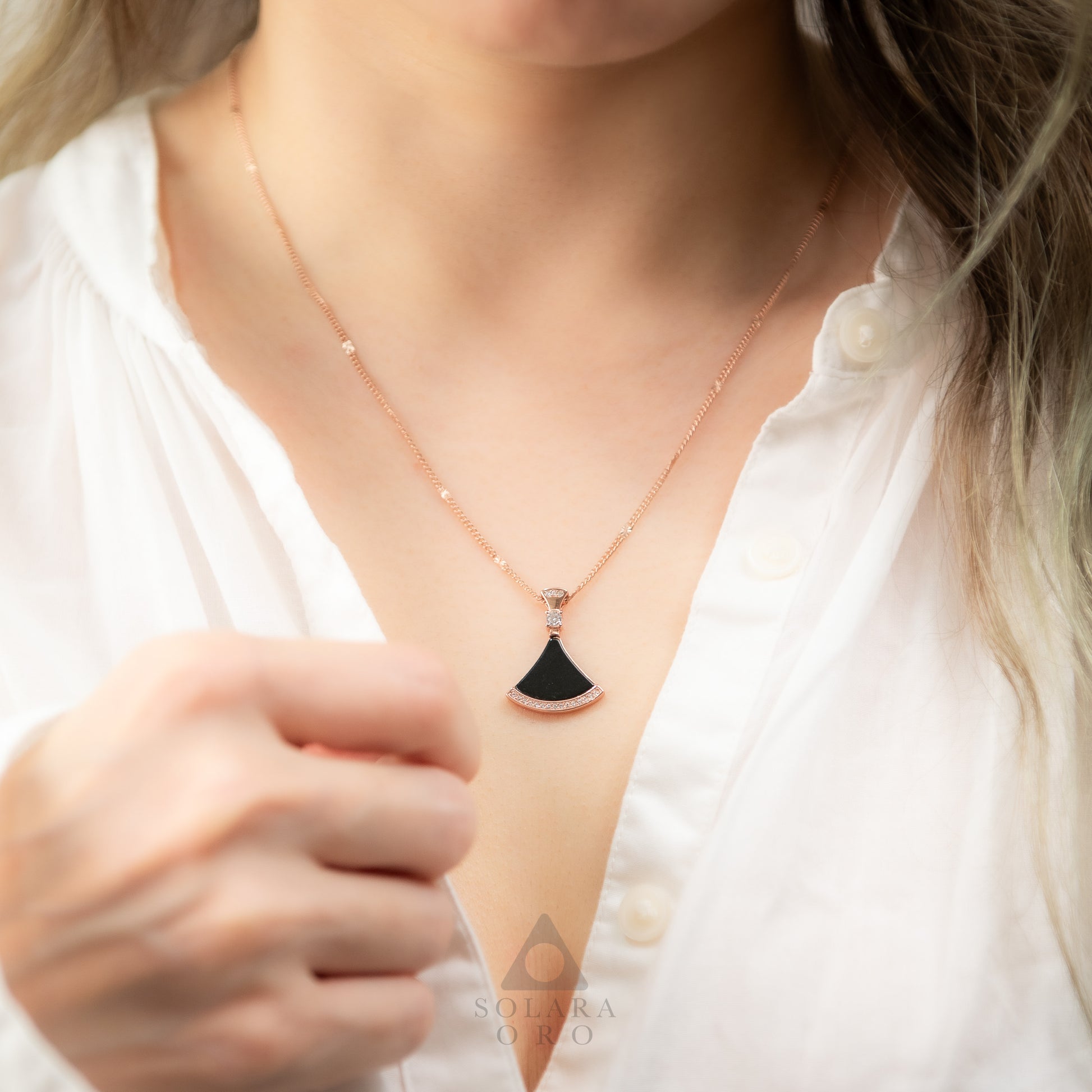 Close-up of a necklace with a black pendant worn by a person in a white shirt.