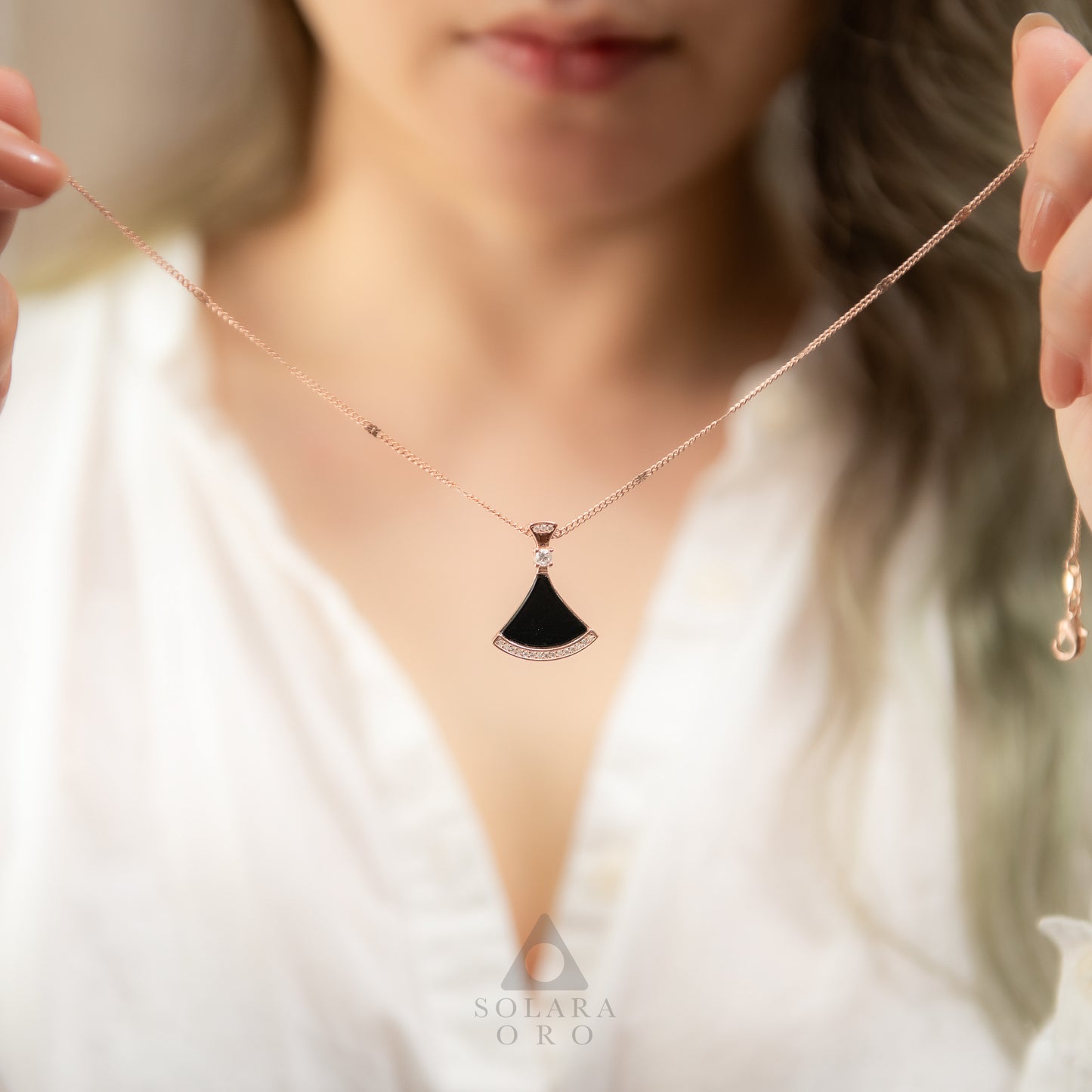Necklace with a black pendant held by a person, brand 'Soleara Oro' visible