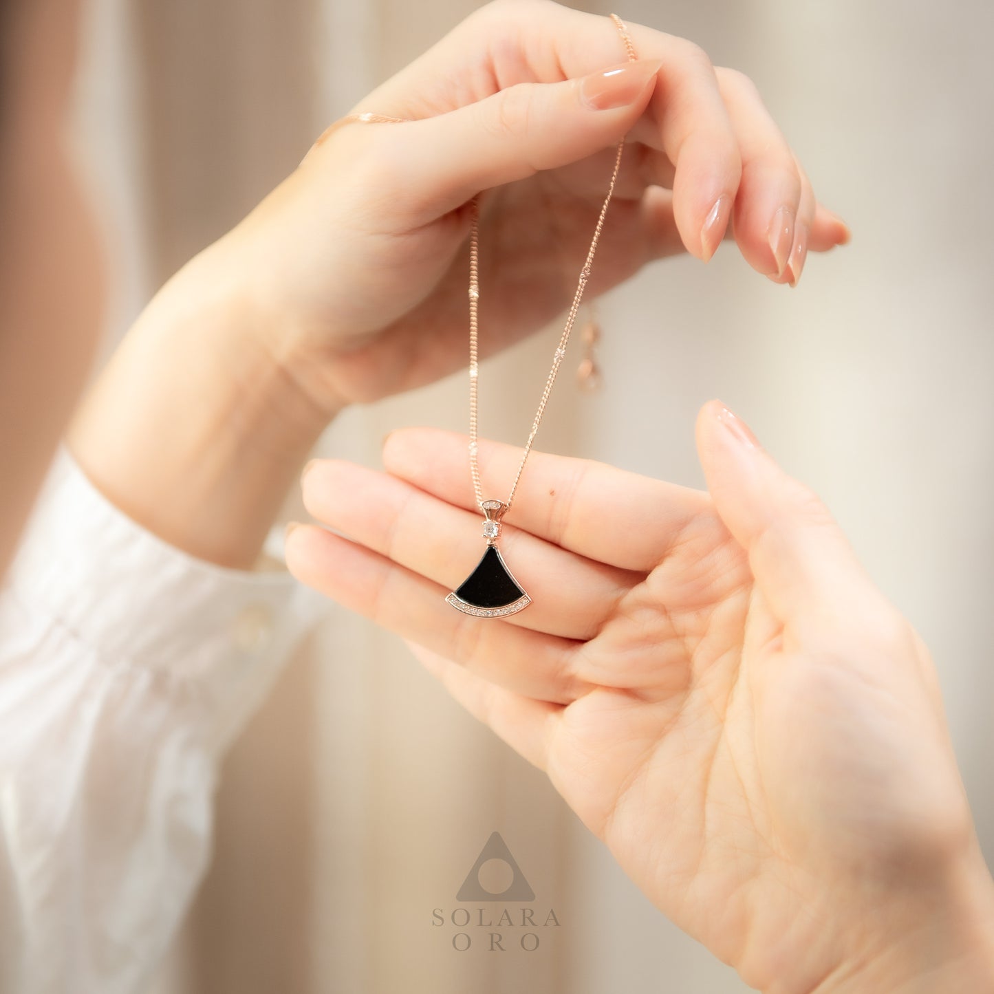 Person holding a necklace with a black pendant, brand 'SOLARA' visible.