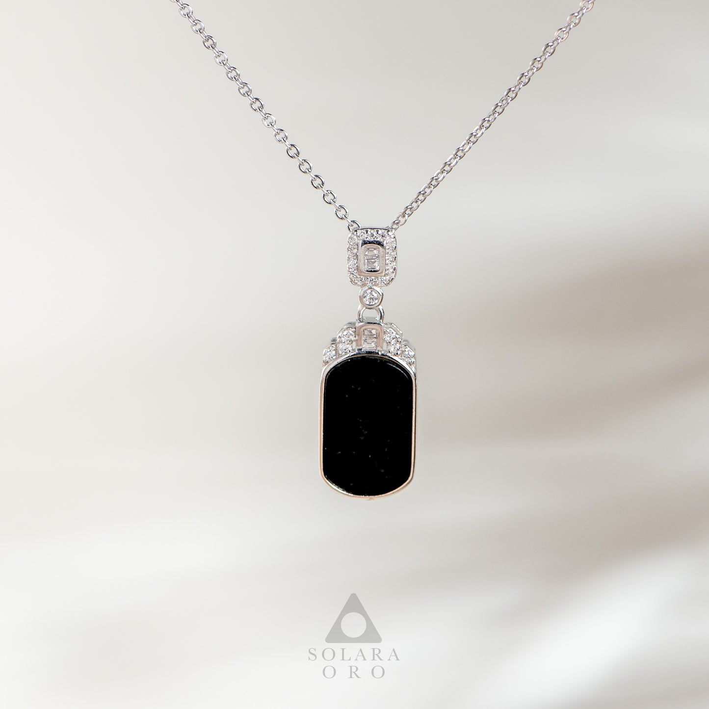 Necklace with a black pendant and silver chain on a soft white background, featuring the Solara Oro brand.
