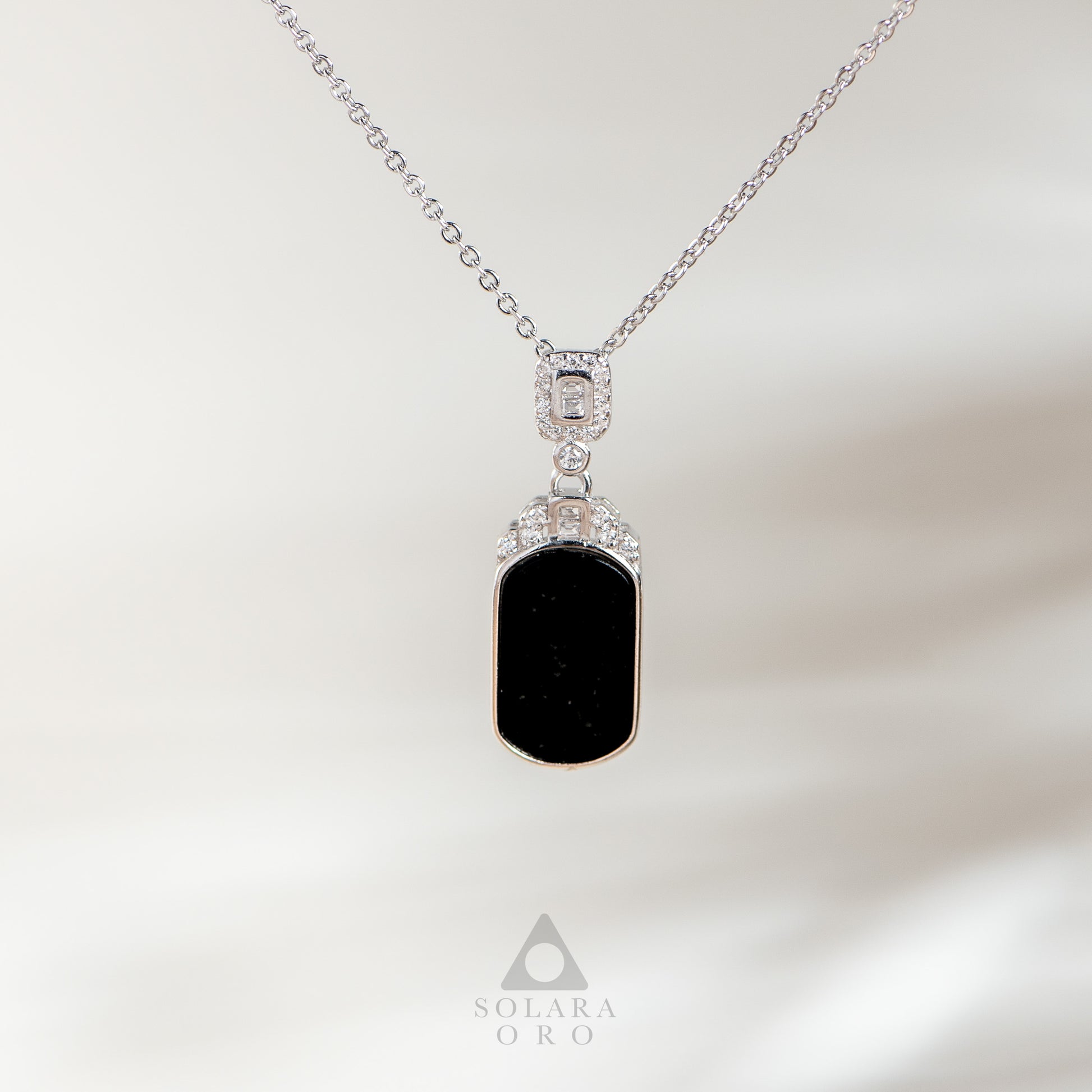 Necklace with a black pendant and silver chain on a soft white background, featuring the Solara Oro brand.