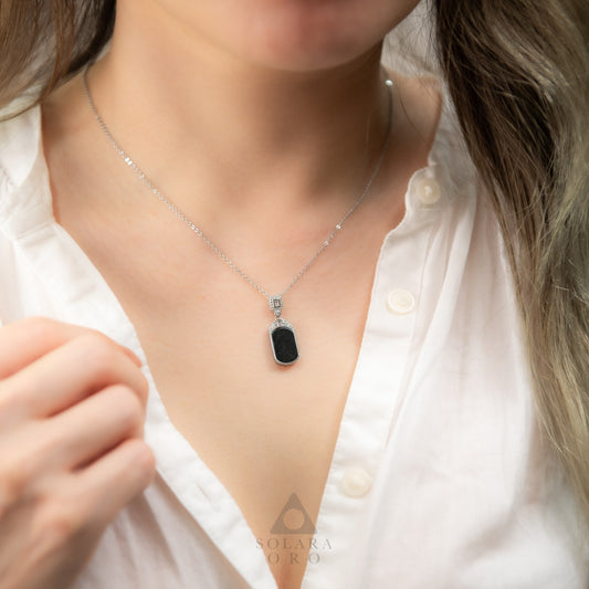 Necklace with a black pendant worn by a person in a white shirt, brand 'Solara Oro' visible.