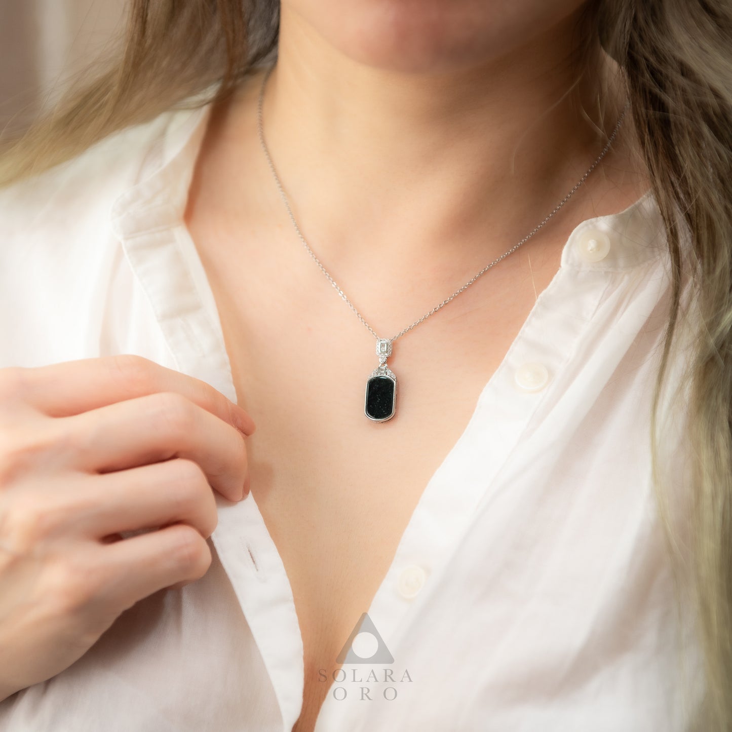 Person wearing a necklace with a black pendant on a plain background