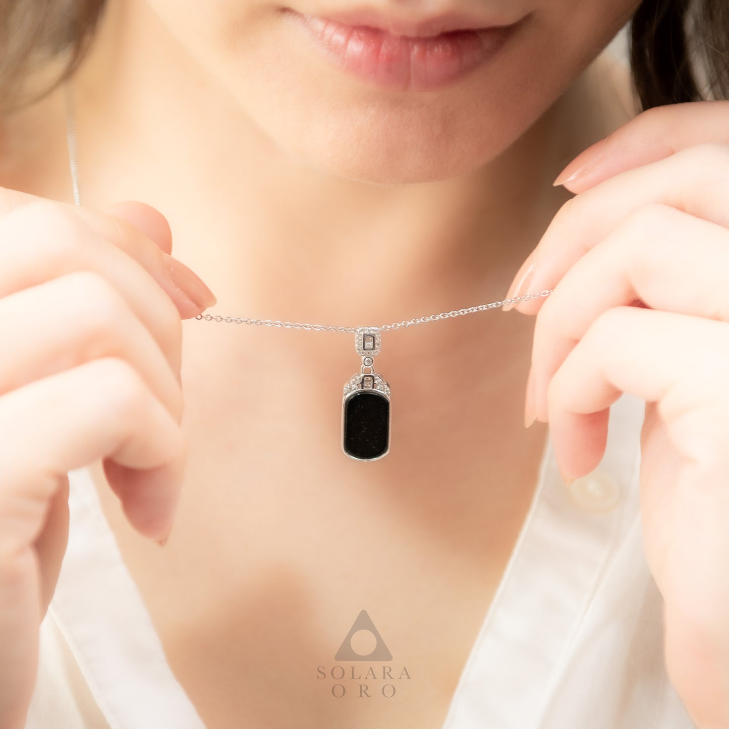 Close-up of a necklace with a black pendant worn by a person, with 'Solara Oro' brand visible.