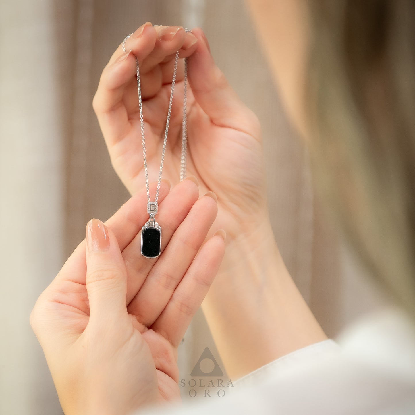 Person holding a necklace with a pendant, brand 'Solara Oro' visible.