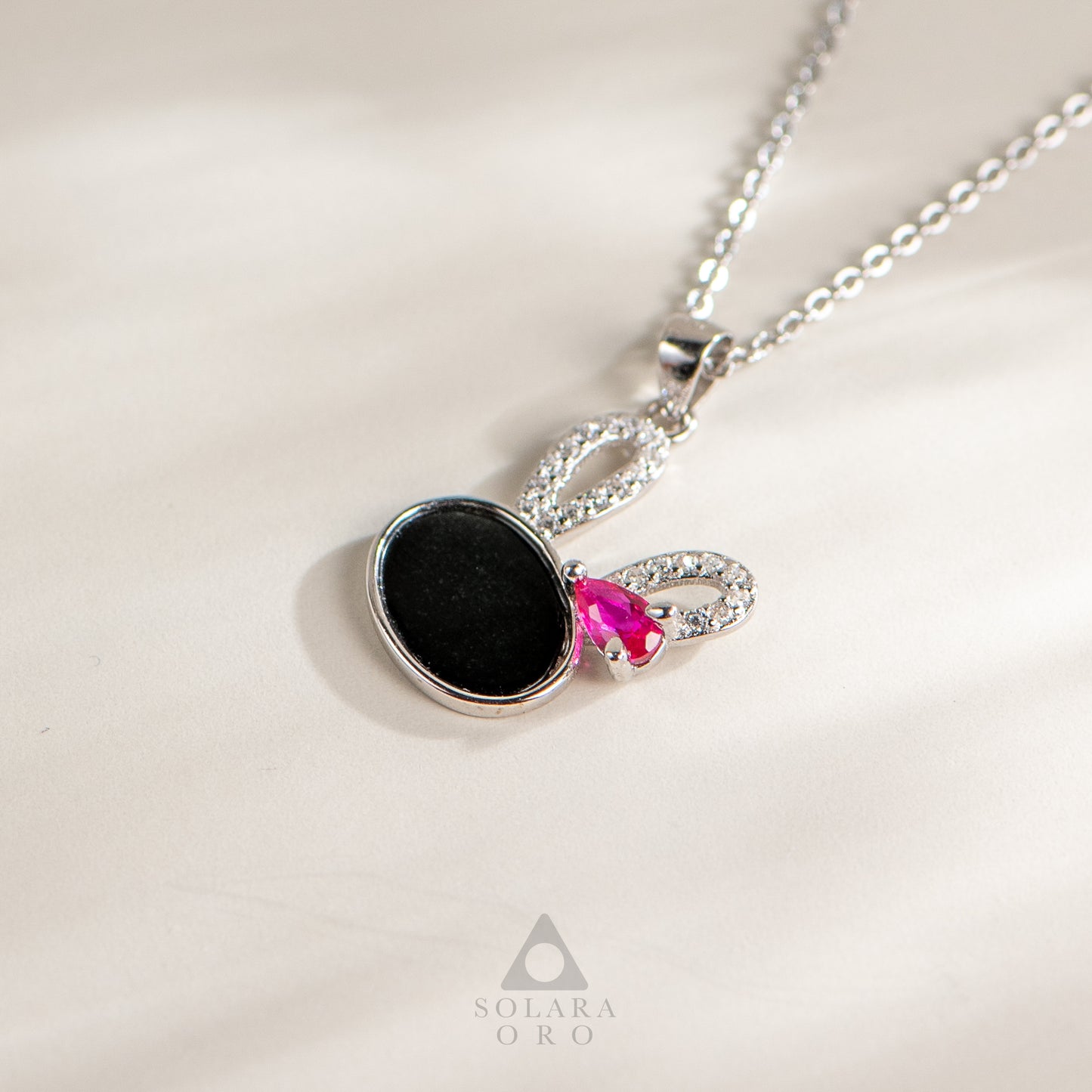 Necklace with black pendant and pink gem on a light background, featuring Solara Oro logo.
