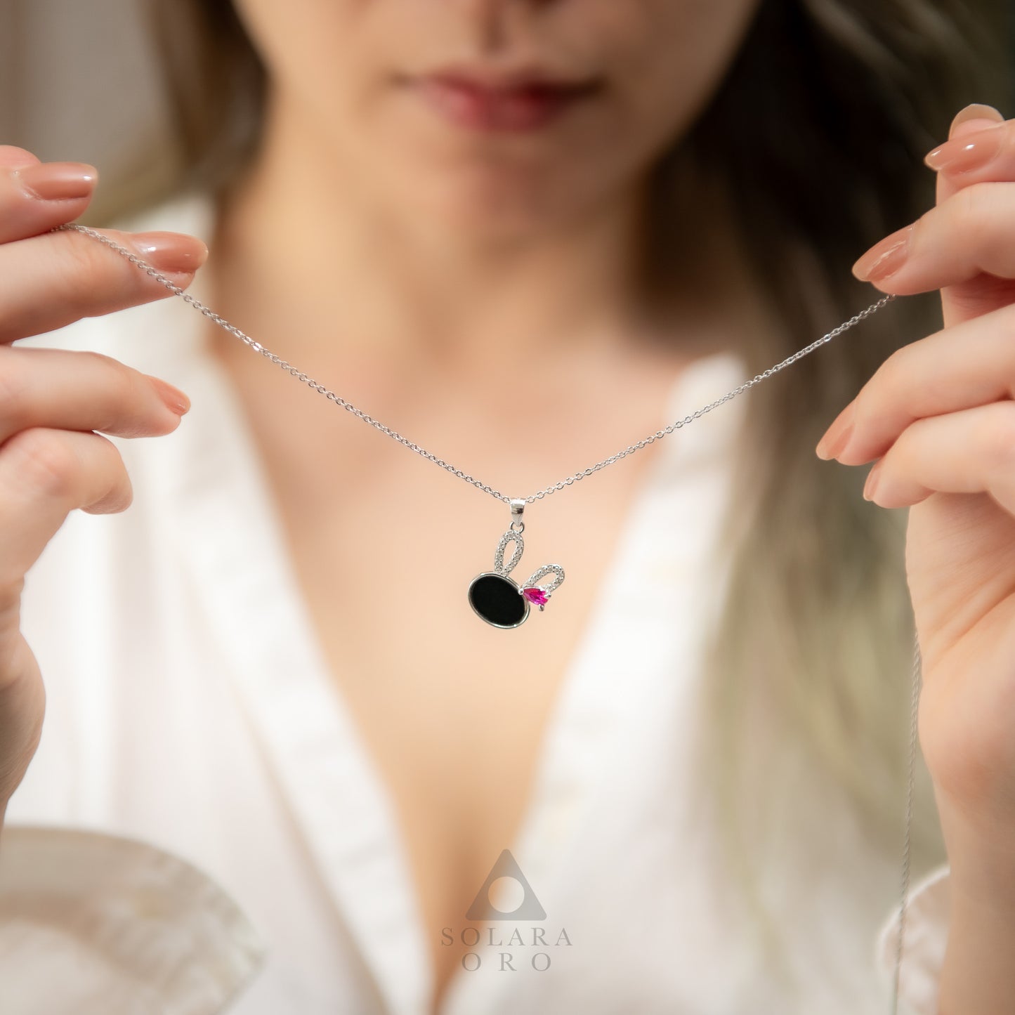 Person holding a necklace with a pendant featuring a black gemstone and pink heart.