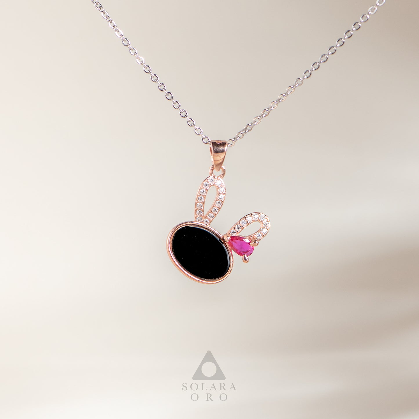 Necklace with a black pendant and pink gemstone on a light background, branded 'Solara Oro'.
