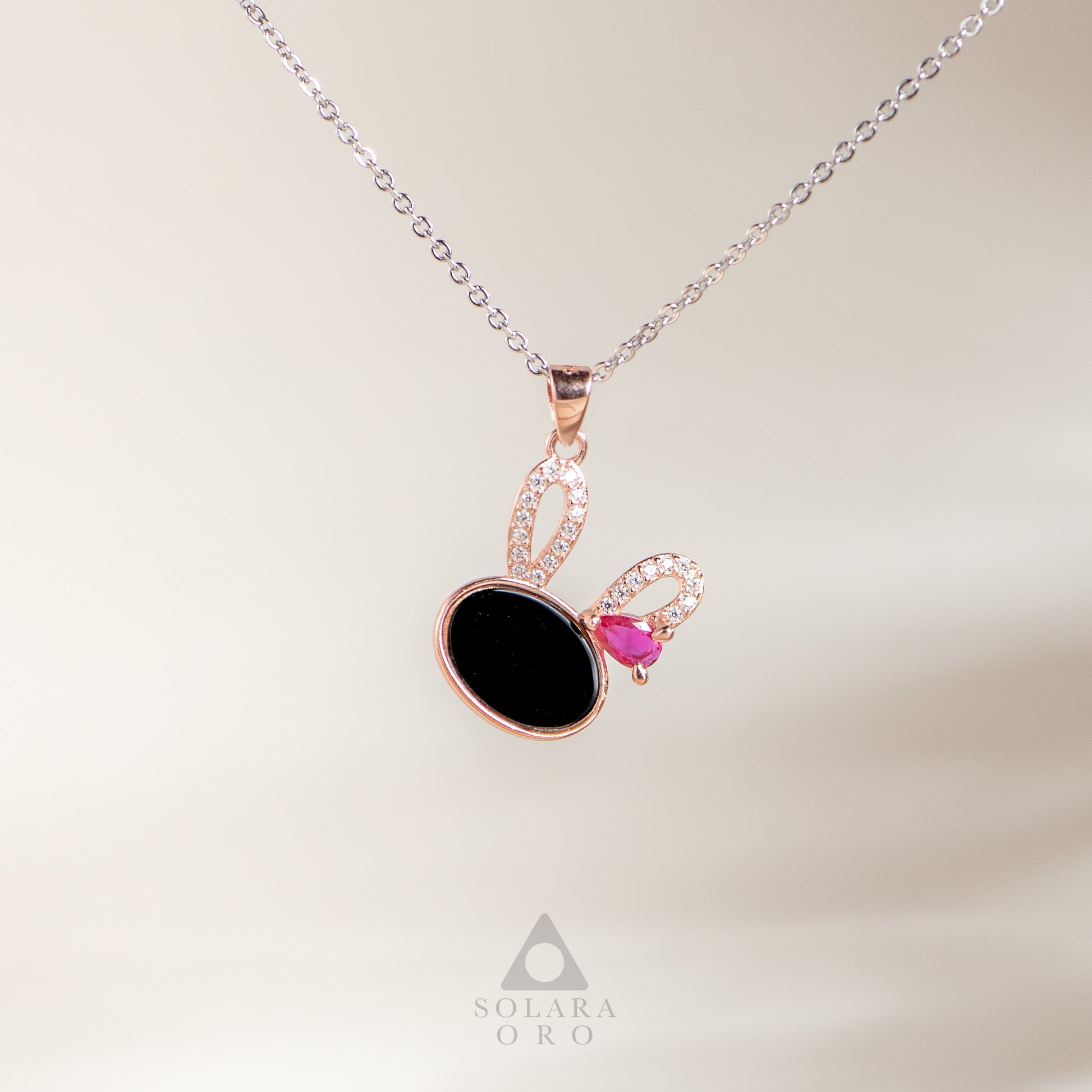 Necklace with a black pendant and pink gemstone on a light background, branded 'Solara Oro'.