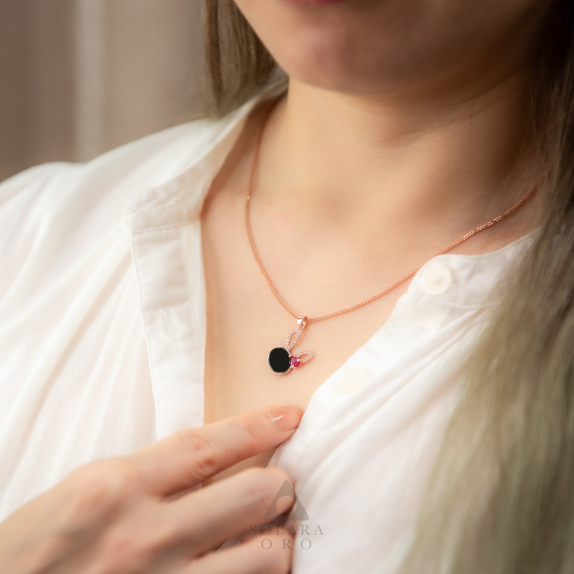 Person wearing a delicate necklace with a black pendant and pink accents.
