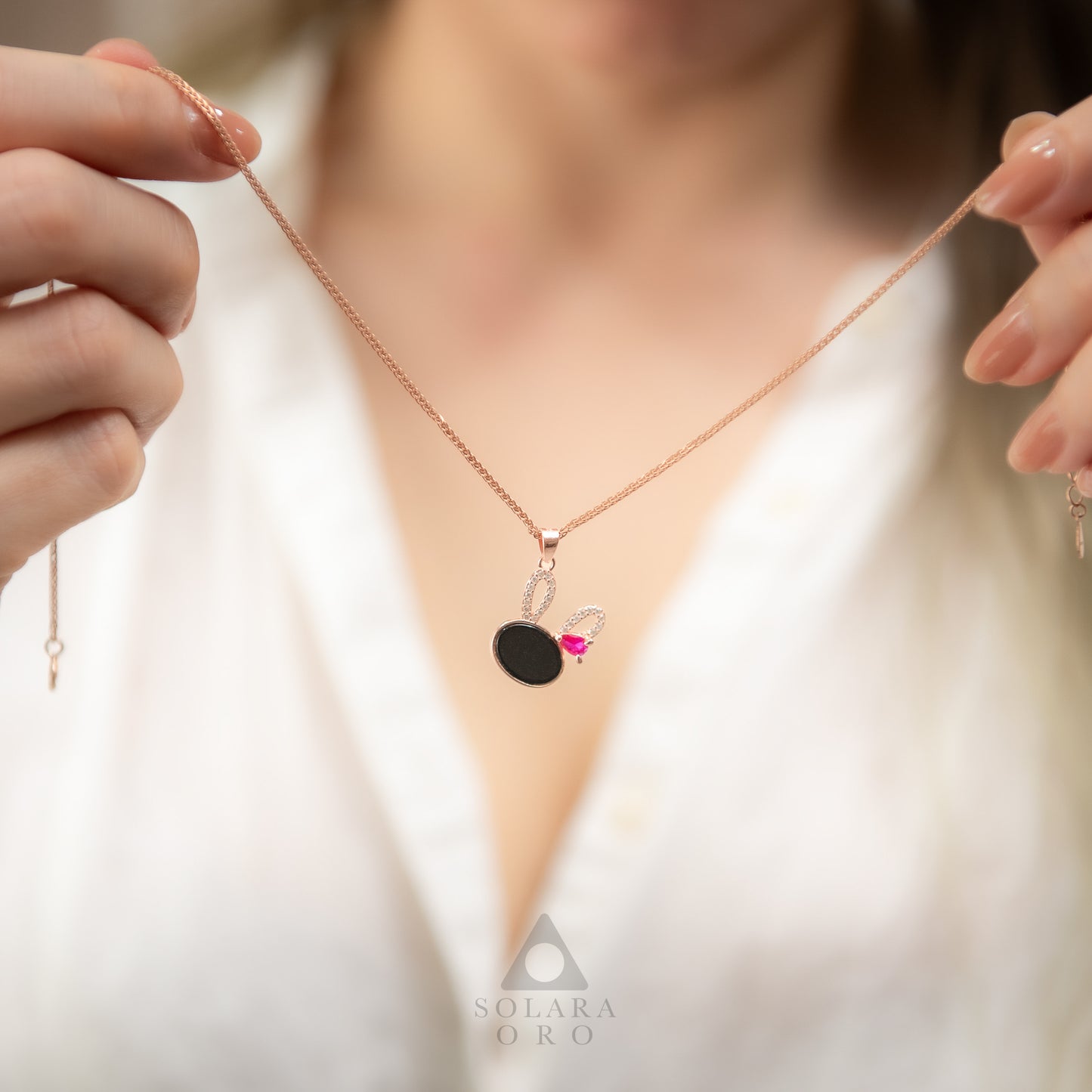 Necklace with a black pendant and pink gemstone held by hands against a blurred background.