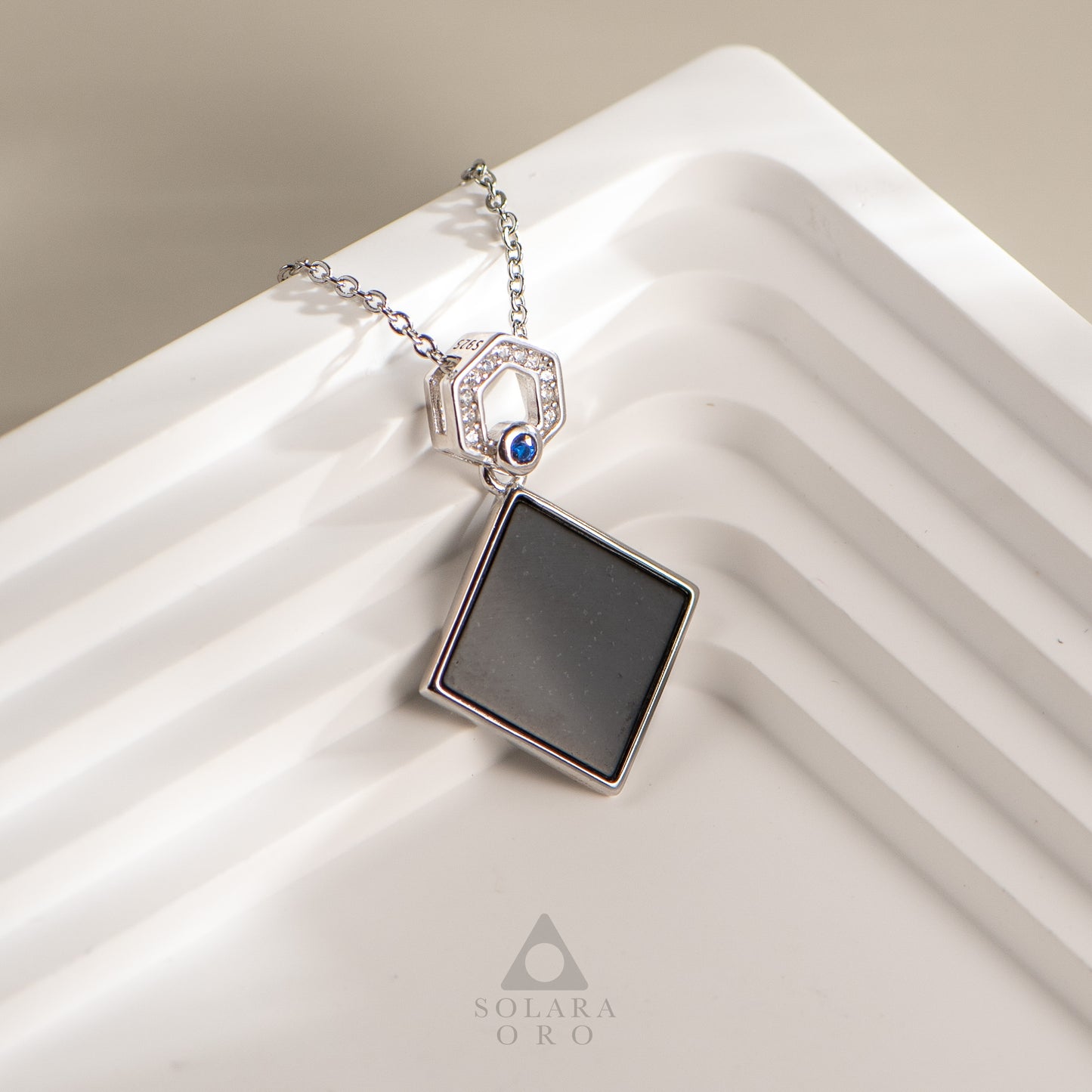 Necklace with a square pendant on a white surface, featuring the brand 'Solara Oro'.