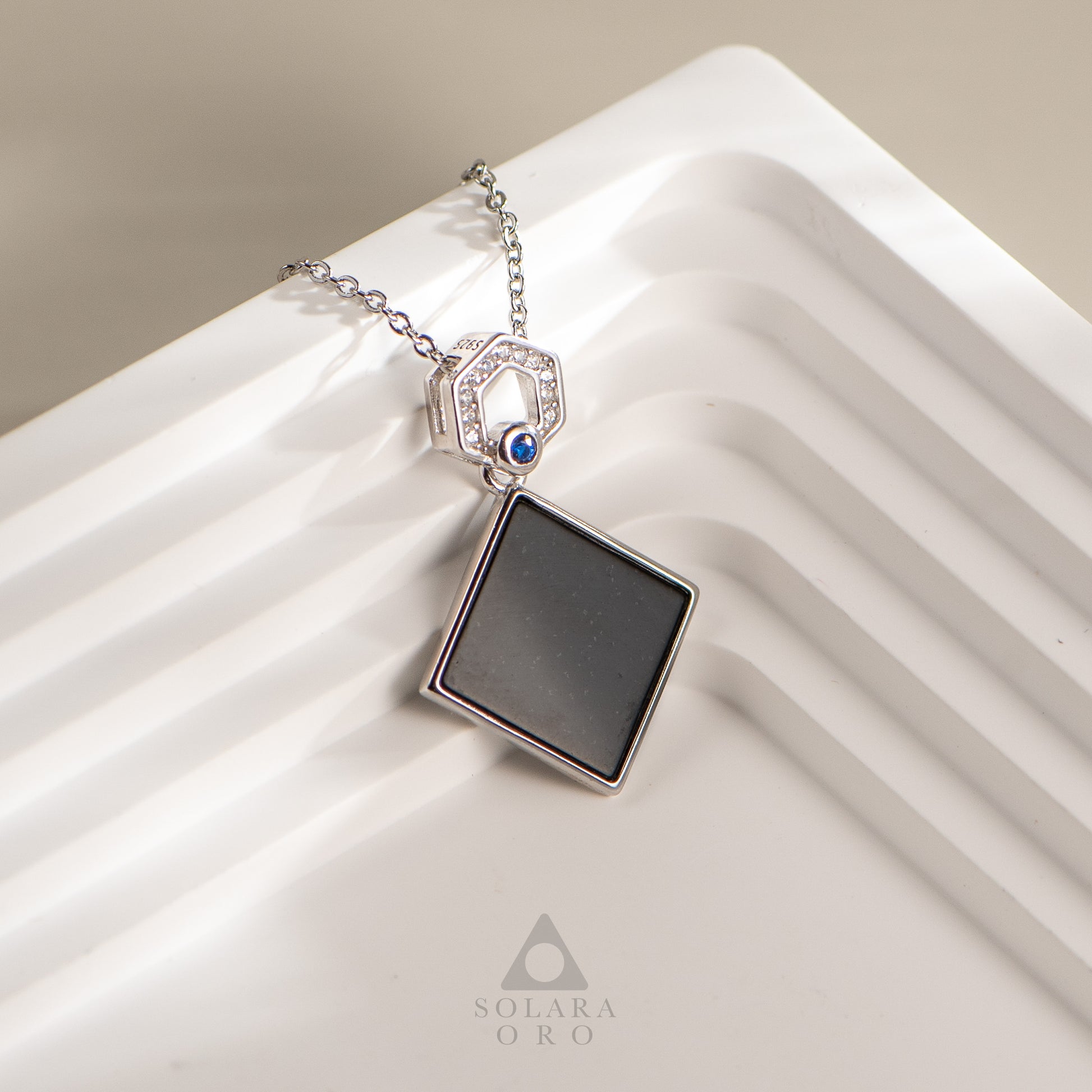 Necklace with a square pendant on a white surface, featuring the brand 'Solara Oro'.