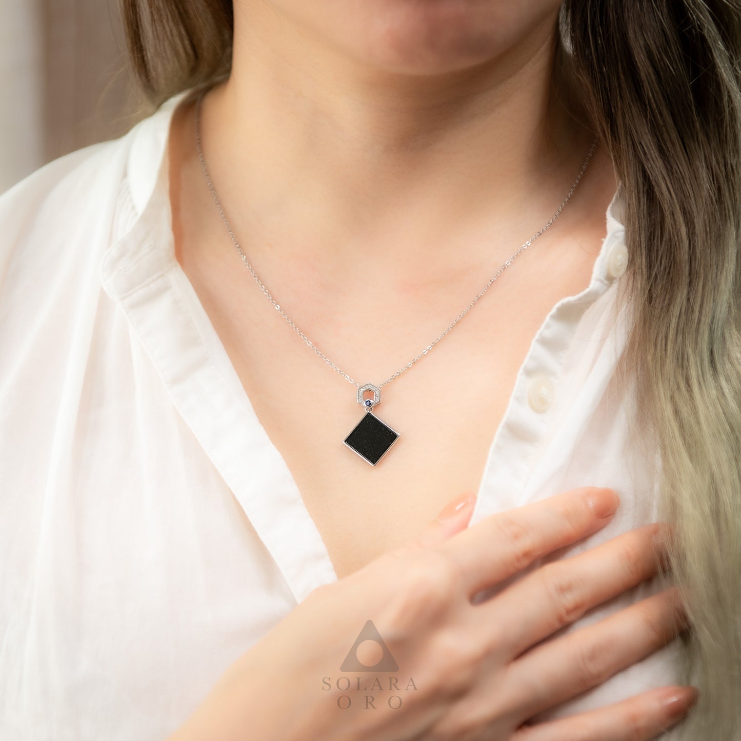 Person wearing a necklace with a black pendant, brand 'Solara Oro' visible.