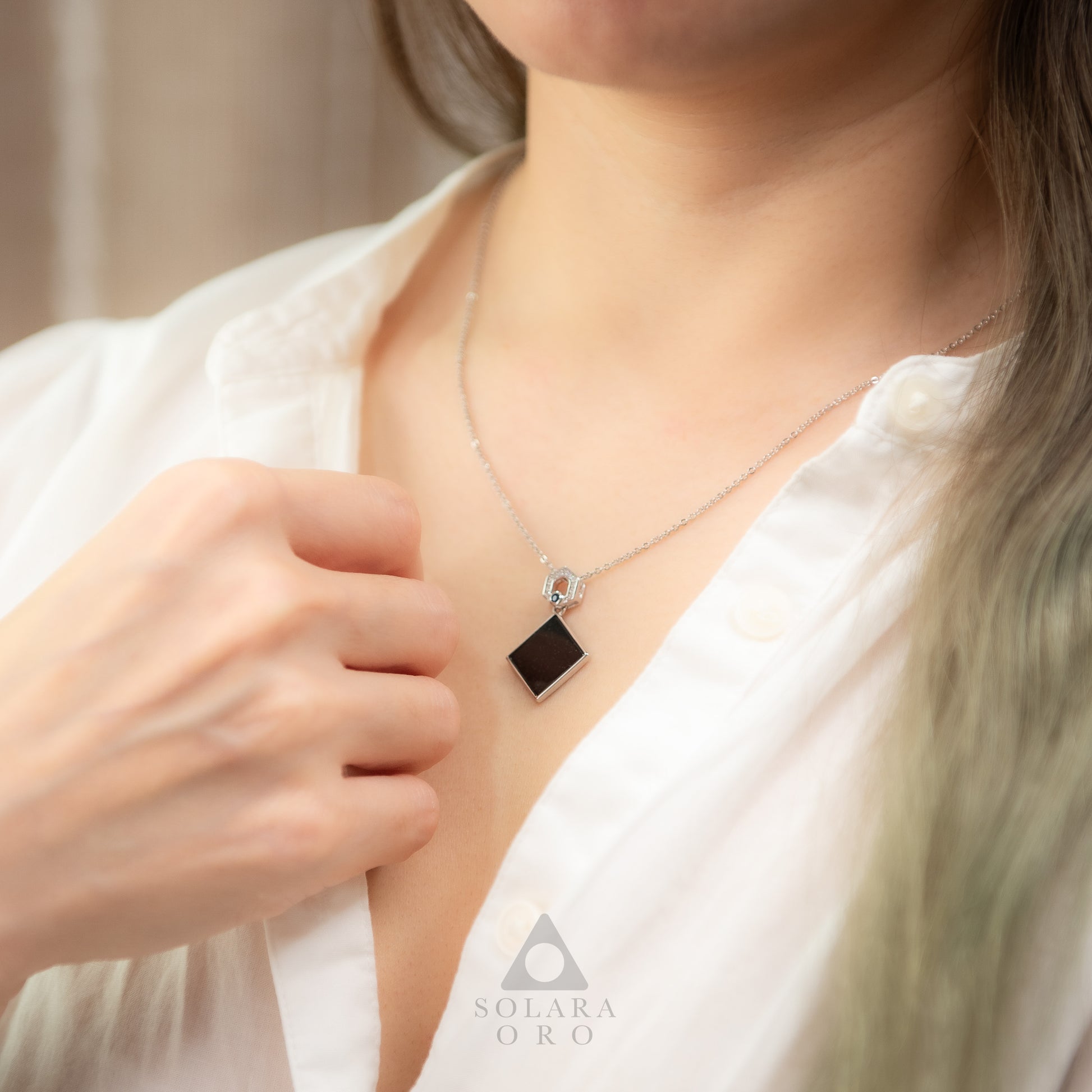 Person wearing a necklace with a pendant, brand 'Solara Oro' visible.
