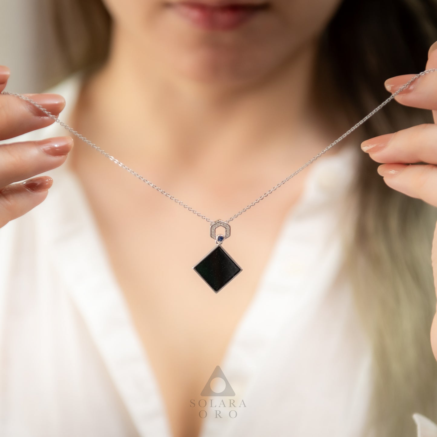 Necklace with a black pendant held by a person, brand 'Solara Oro' visible.