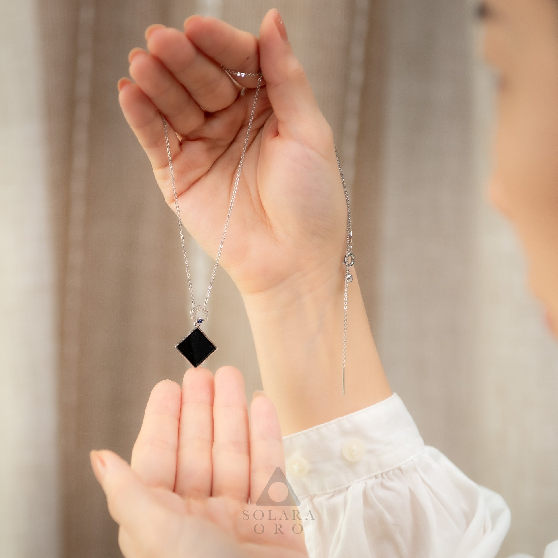 Person holding a delicate necklace with a black pendant against a neutral background