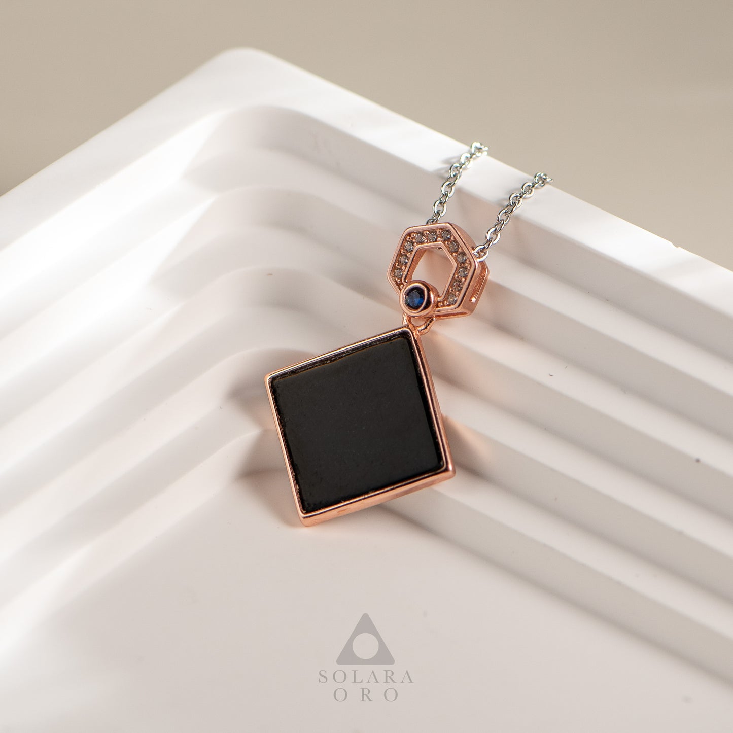 Necklace with a black square pendant and rose gold accents on a white surface, featuring the brand 'Solara Oro'.