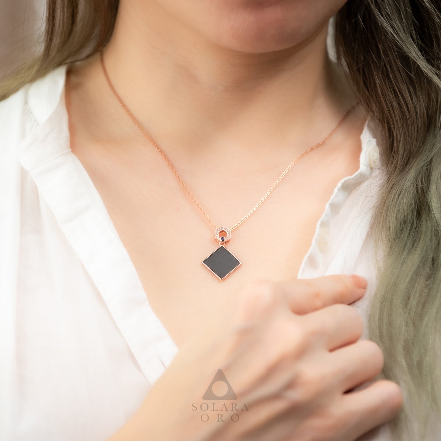 Necklace with a black pendant worn by a person, brand 'Solara Oro' visible.