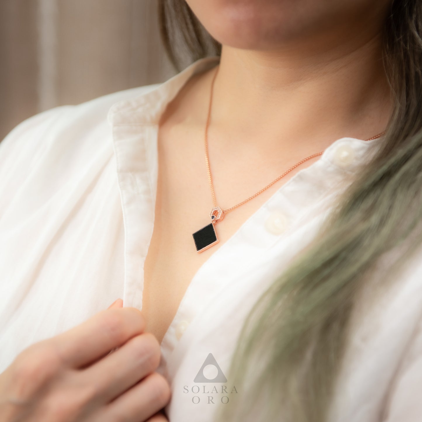 Person wearing a necklace with a black pendant, brand 'Solara Oro' visible.