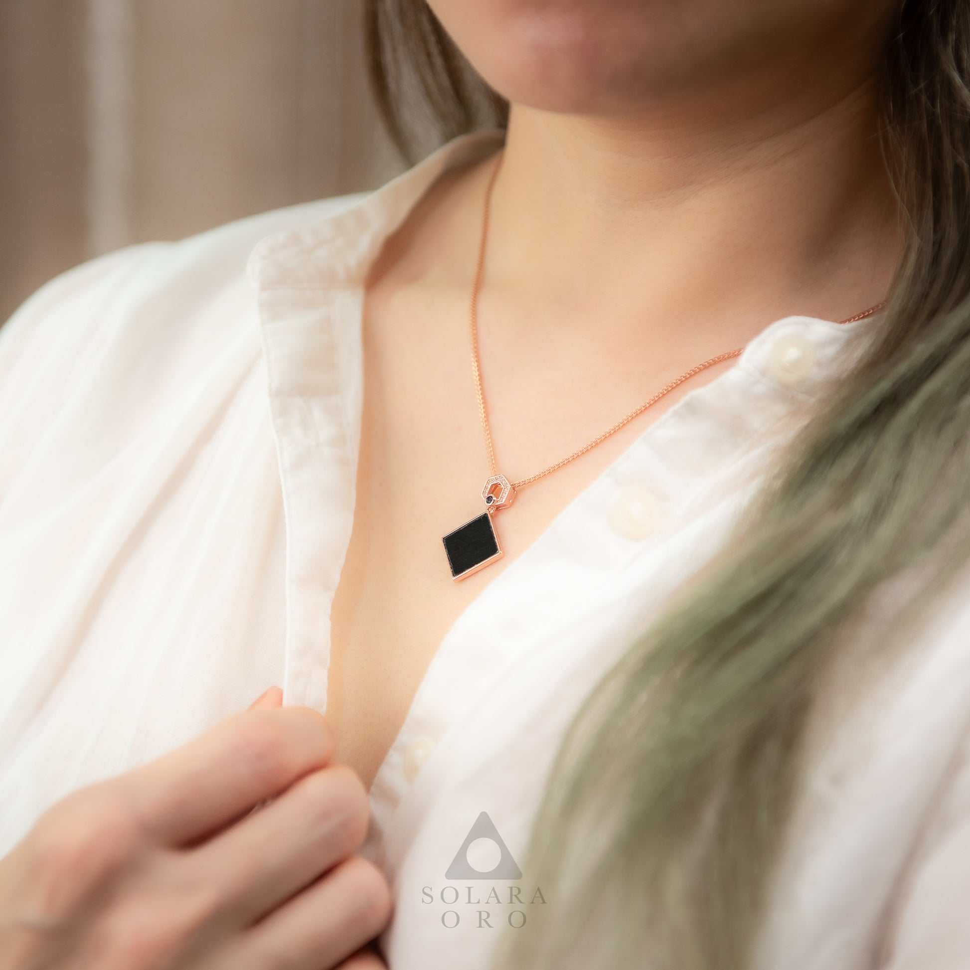Person wearing a necklace with a black pendant, brand 'Solara Oro' visible.