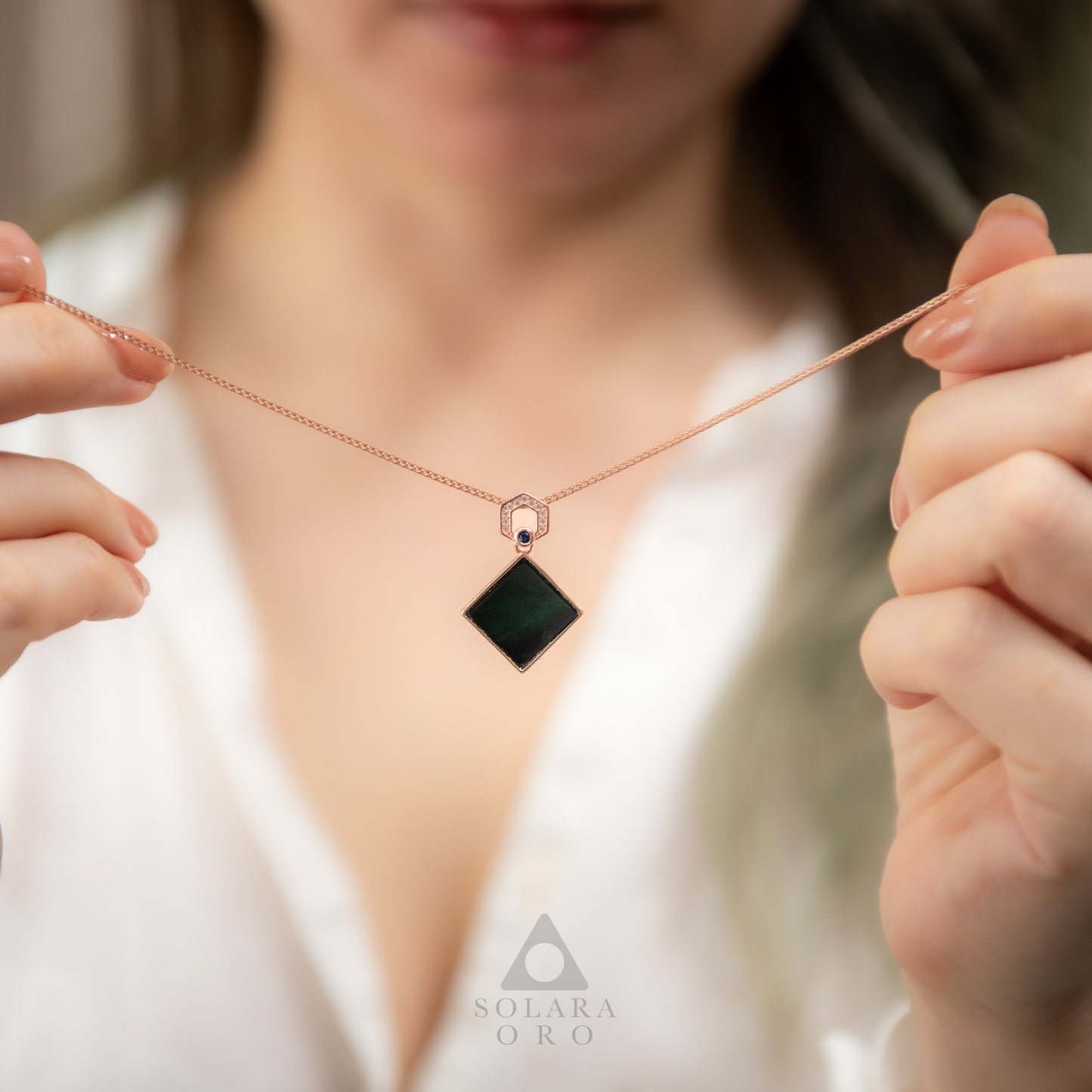Person holding a necklace with a black pendant and rose gold chain, brand 'Soleara Oro' visible.